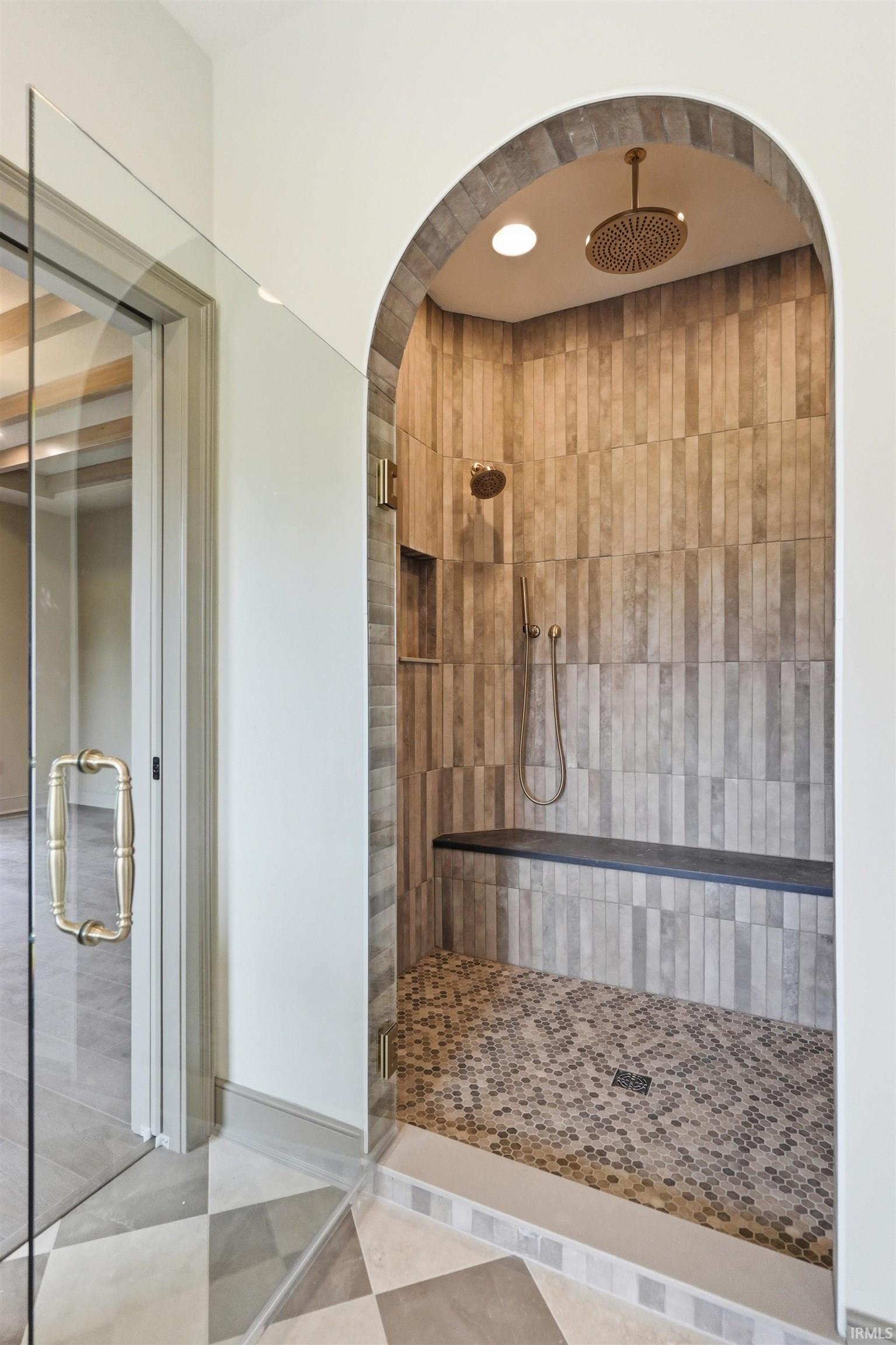 Arched shower entry featuring vertical tile walls, penny tile flooring, and a built-in bench
