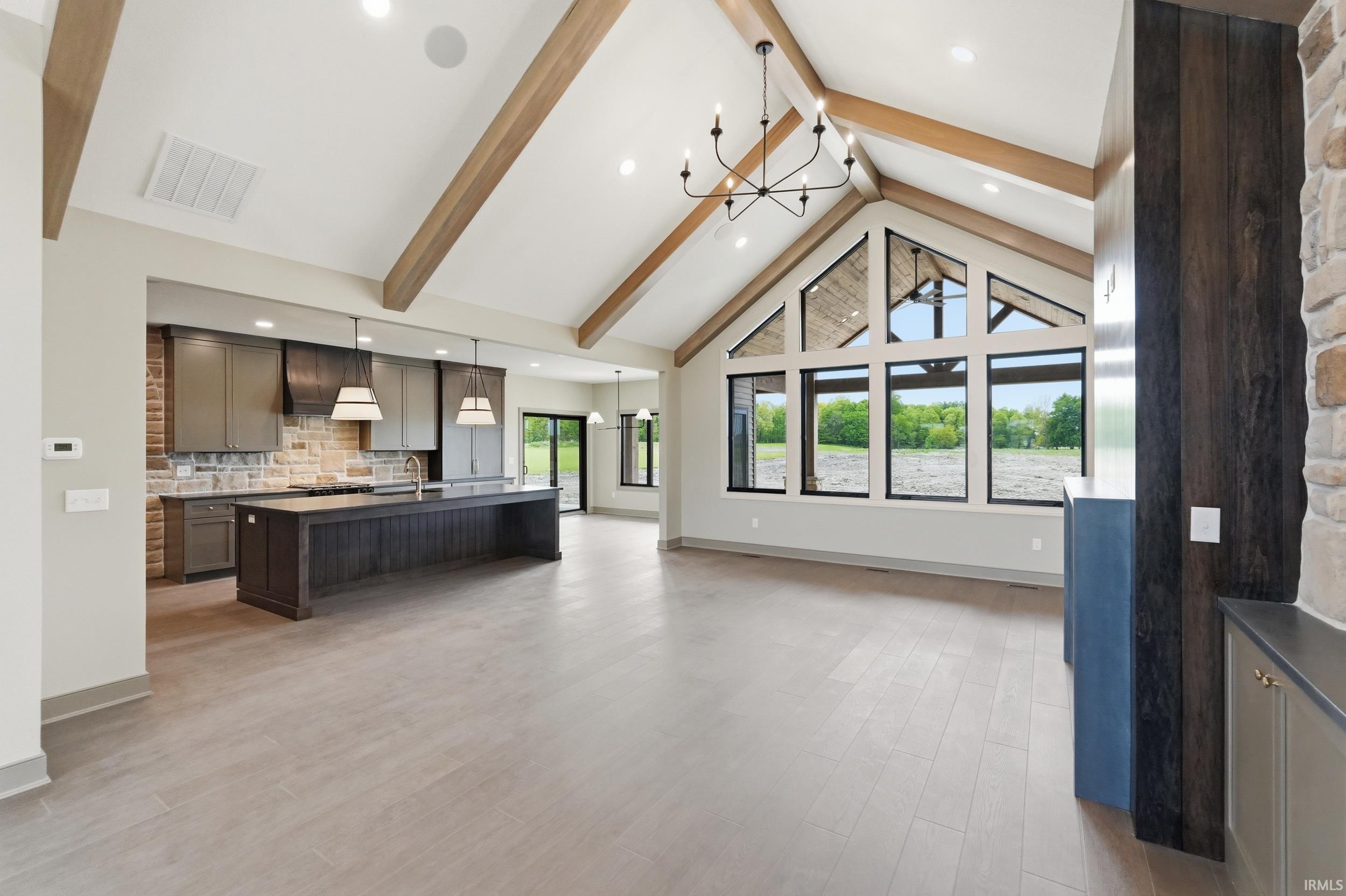 Vaulted ceilings with exposed wood beams, expansive floor-to-ceiling windows, and light wood-finish flooring define this open-concept living space