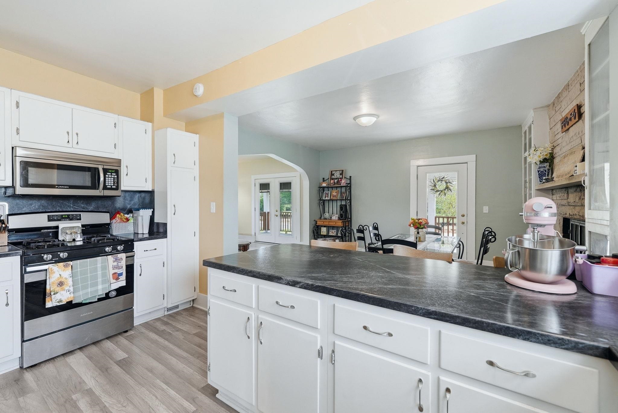 Kitchen featuring white cabinetry, dark countertops, a stainless steel oven/range, a built-in microwave, and wood-finish flooring