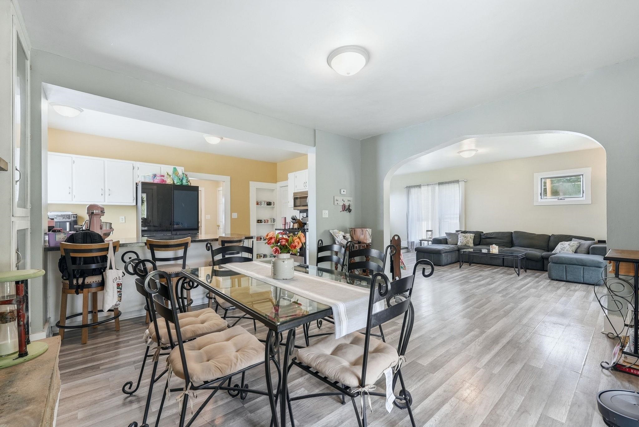 Open-concept living space featuring wood-finish flooring, recessed lighting, a breakfast bar, white cabinetry, and an arched entryway