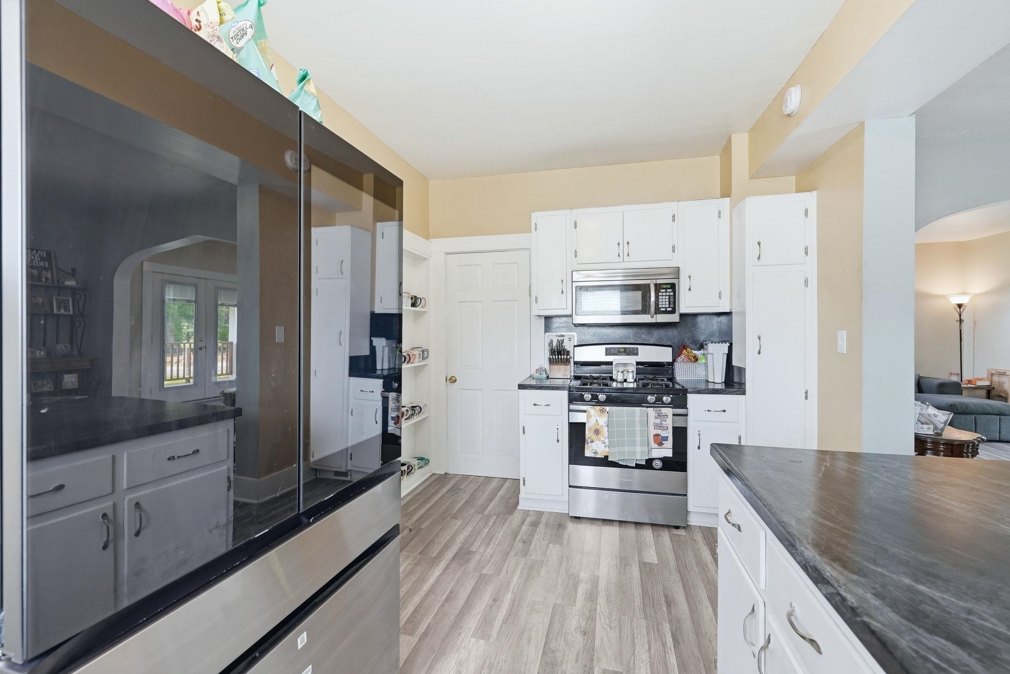 Kitchen featuring wood-finish flooring, white cabinetry, dark countertops, and stainless steel appliances including a range and microwave