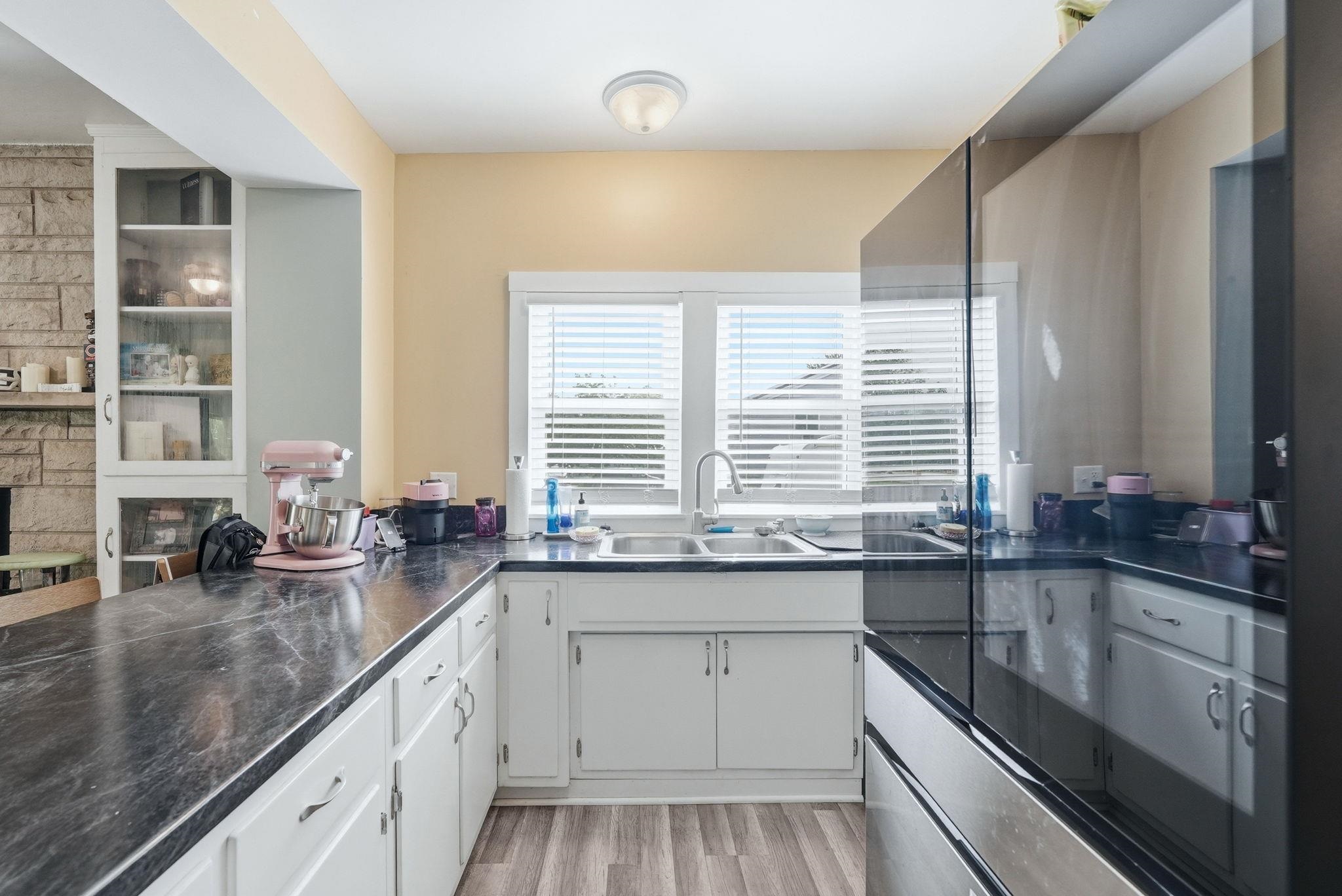 Kitchen featuring wood-finish flooring, white cabinetry, dark countertops, a double basin sink with a gooseneck faucet, and a large window with blinds