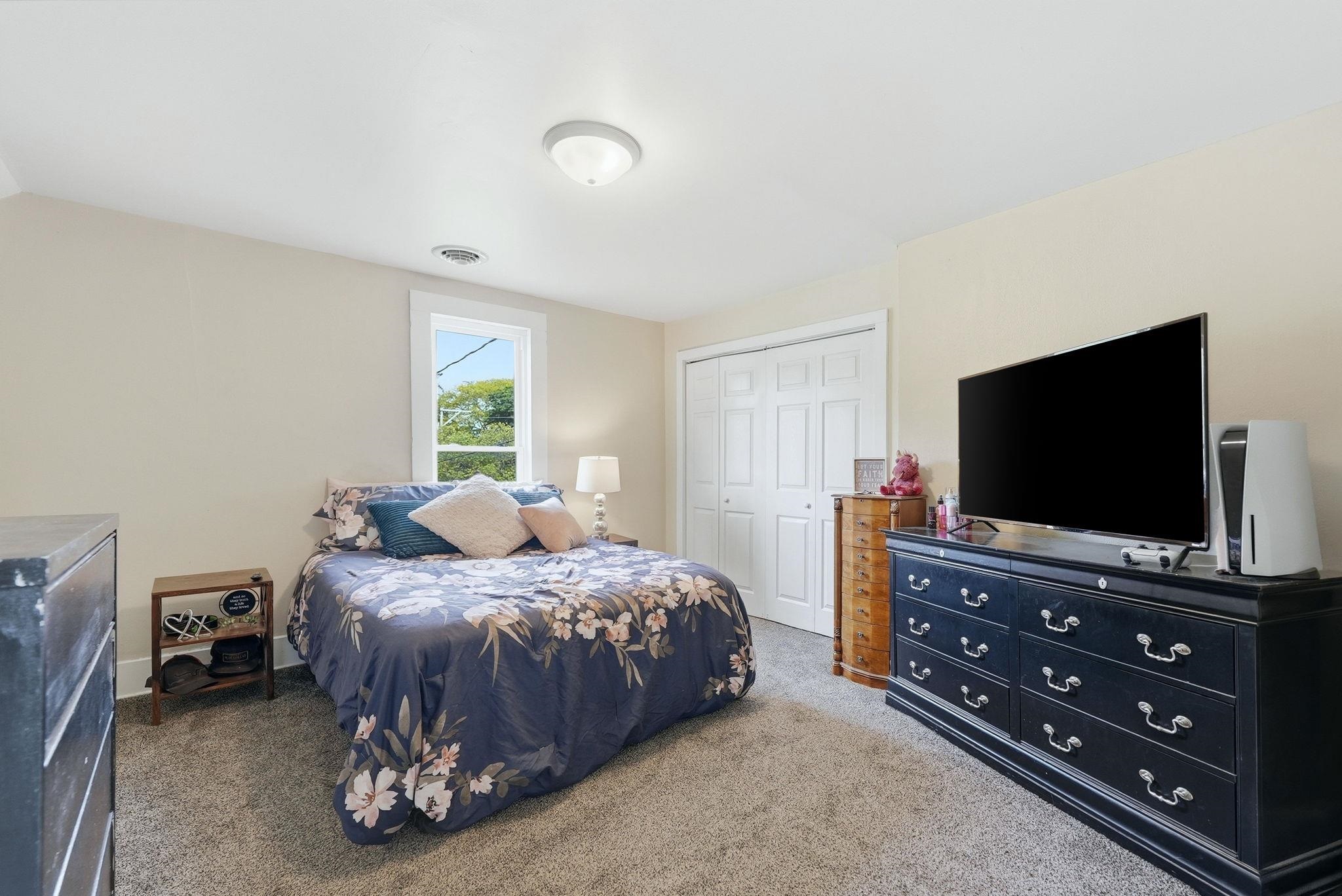 Carpeted room with neutral-toned walls, a white trim window, a ceiling-mounted light fixture, and a bi-fold closet door