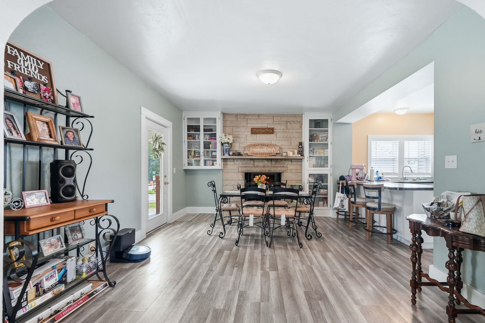 Light wood-finish flooring throughout, a stone-front fireplace with built-in cabinetry, an arched doorway, and an open-concept living space