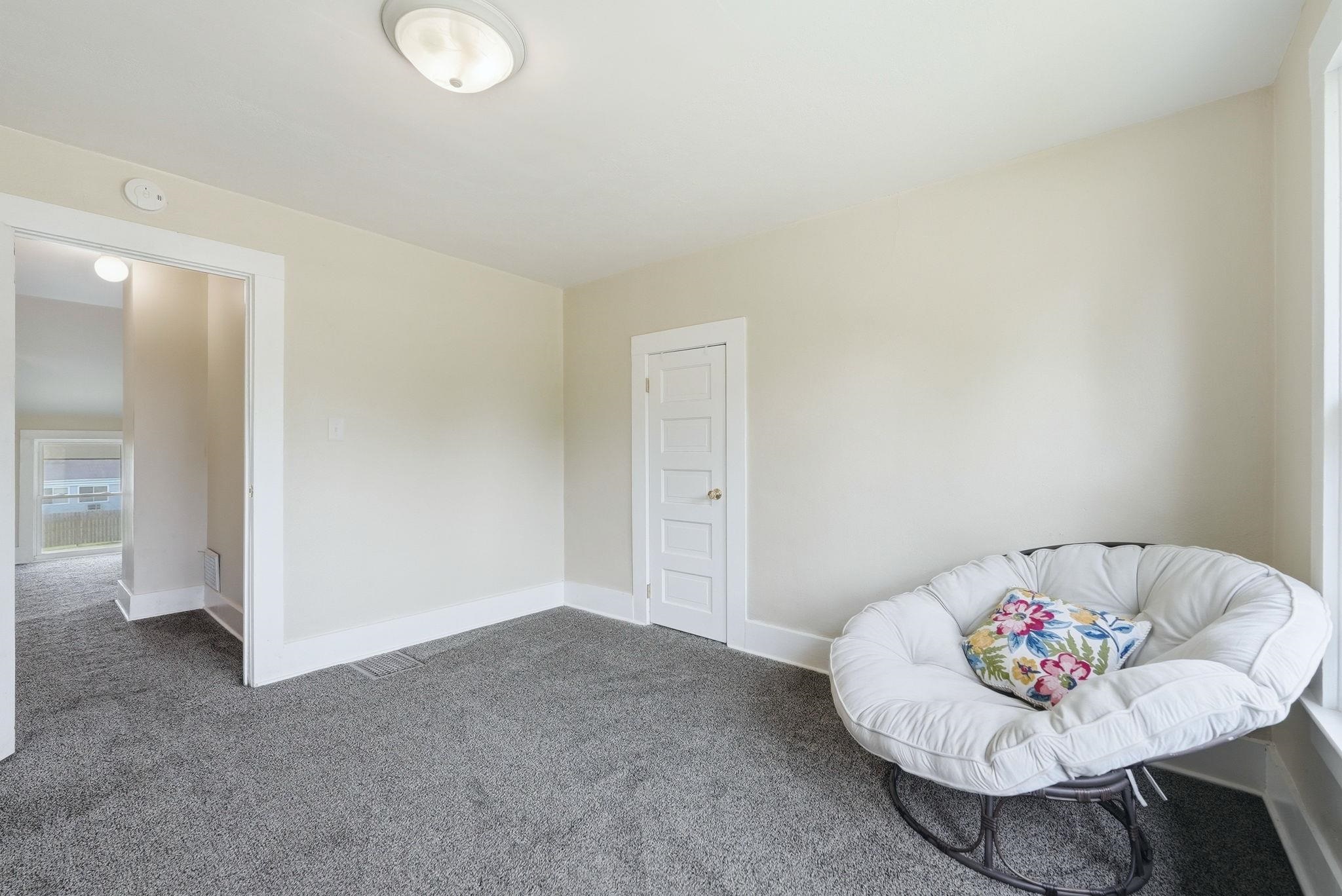 Carpeted room featuring a white five-panel interior door with a brass-finish knob, white baseboards, and neutral wall paint