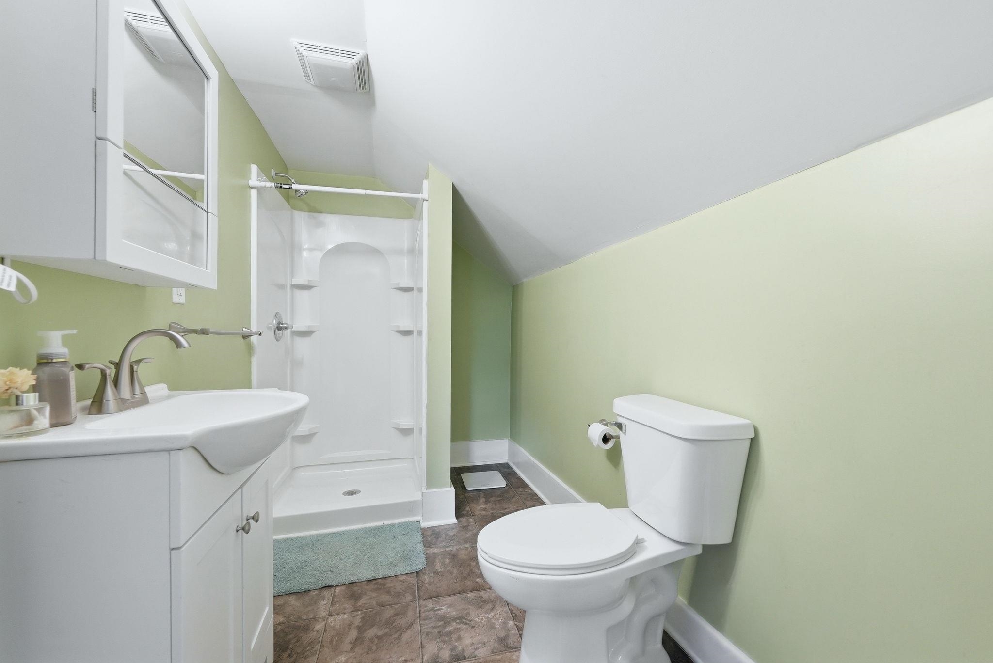 Bathroom featuring a white vanity with integrated sink, brushed nickel faucet, a stand-up shower with a white surround, and a white toilet