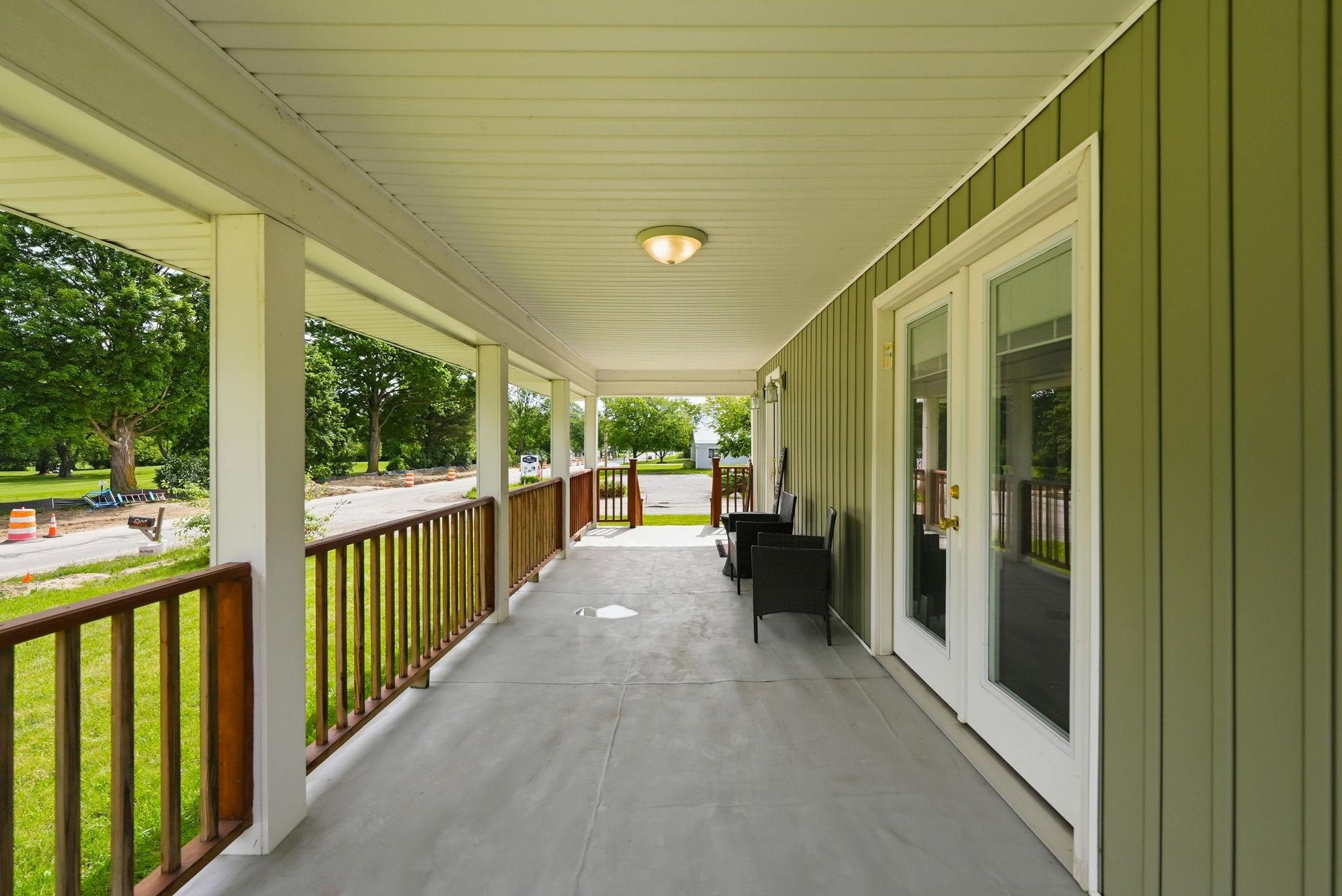 Expansive covered porch featuring a concrete surface, painted support columns, wood railings, and a beadboard ceiling