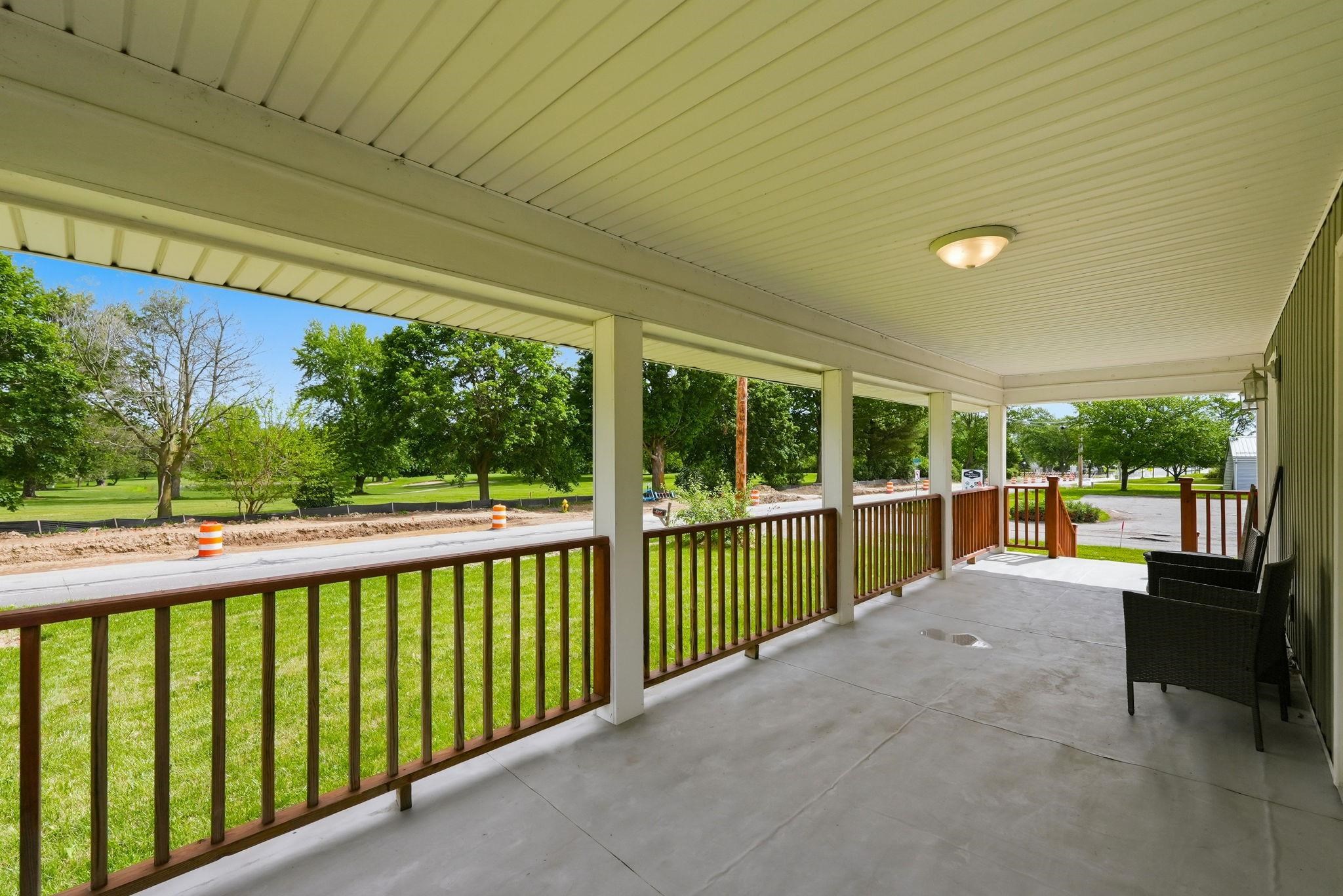 Spacious covered front porch with a concrete surface, white columns, and wood-finish railings