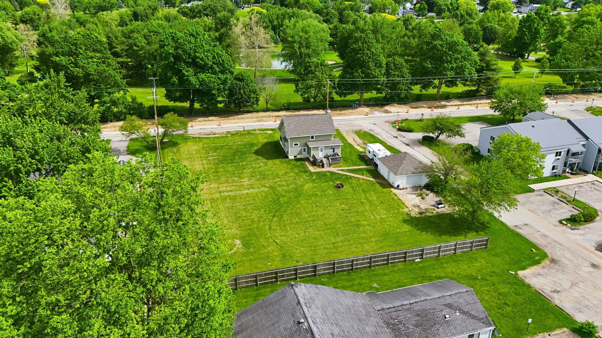 Spacious property featuring a detached residence with light gray siding, a large manicured lawn, a detached garage, and perimeter fencing