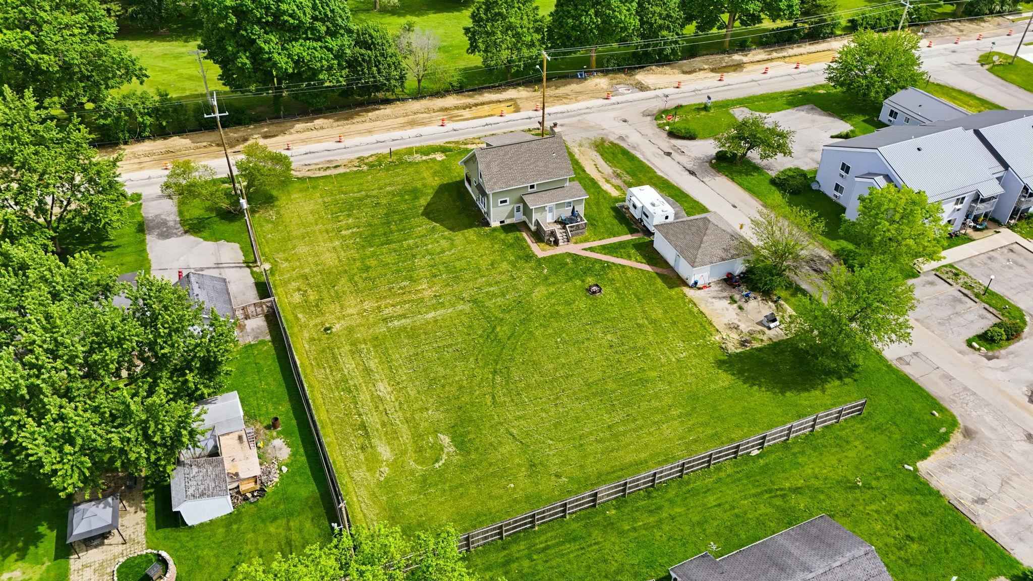 Expansive green lot featuring a two-story residence with a gabled roof, an attached covered porch, a detached garage, and partial perimeter fencing