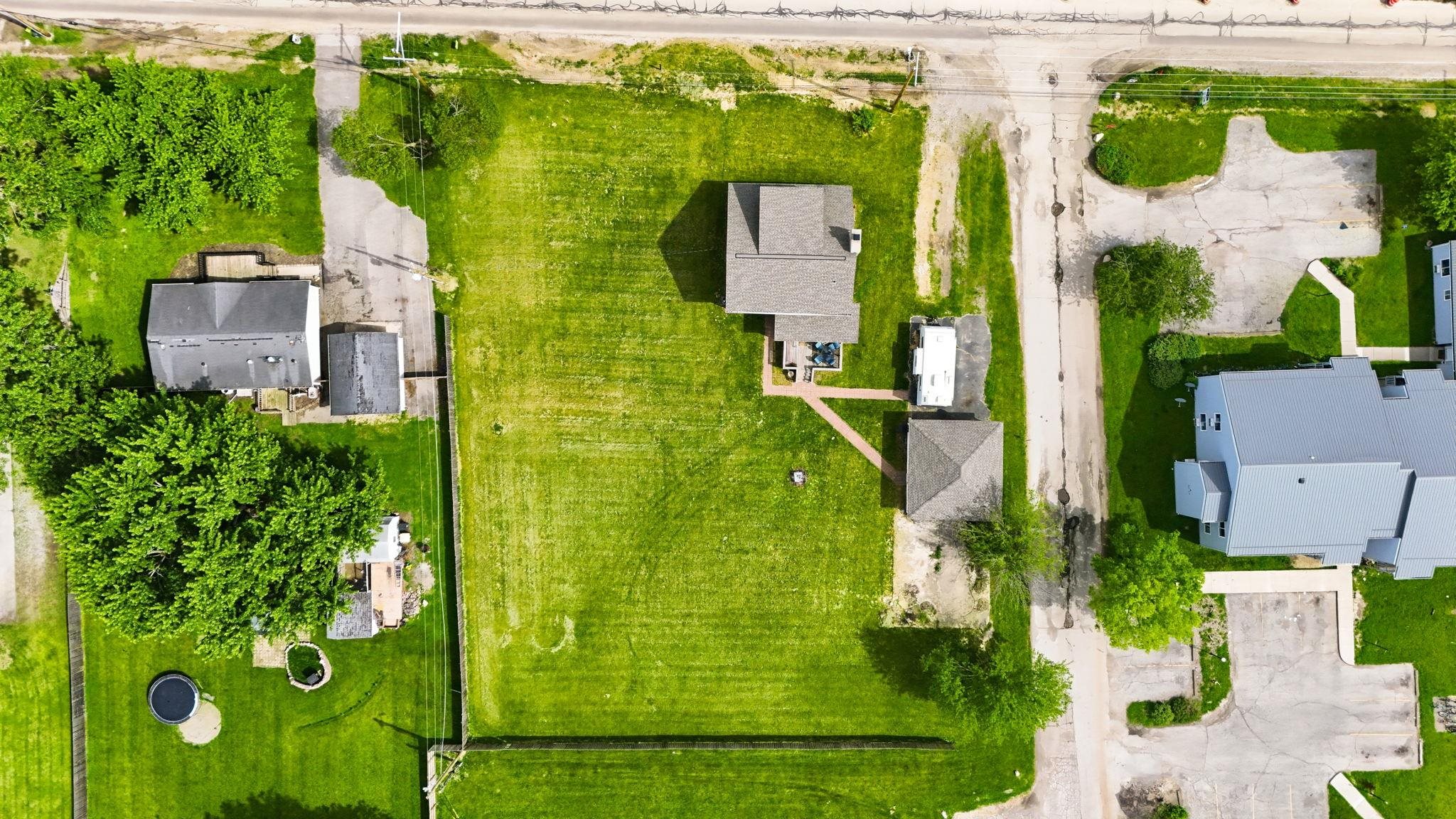 Residential property featuring a main house with a gray shingle roof, an additional detached structure with a matching roof, a gravel driveway, and expansive grassed areas