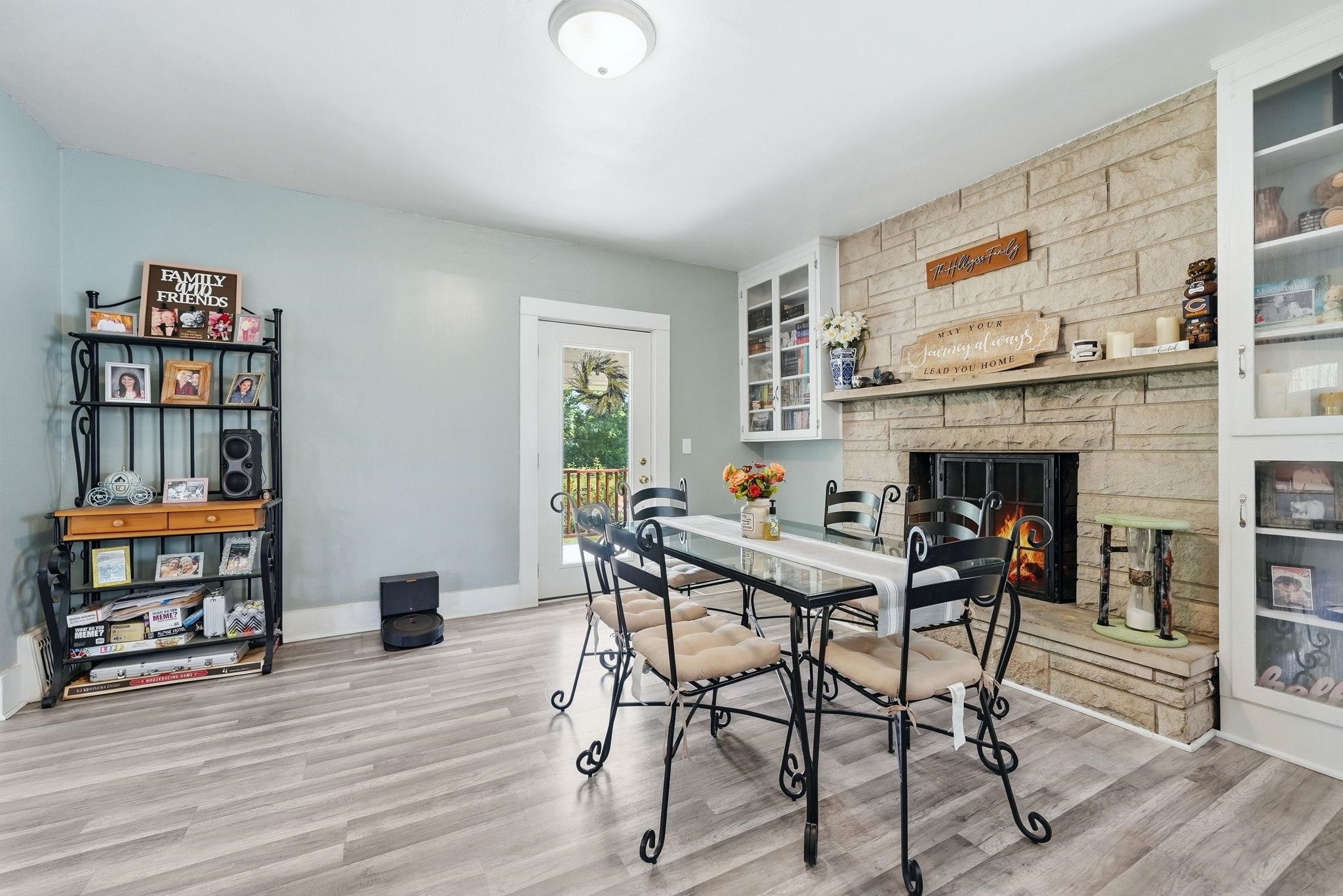 Dining area featuring a stone-clad fireplace, wood-finish flooring, a white trim doorway with glass paneling, and built-in glass-front cabinetry