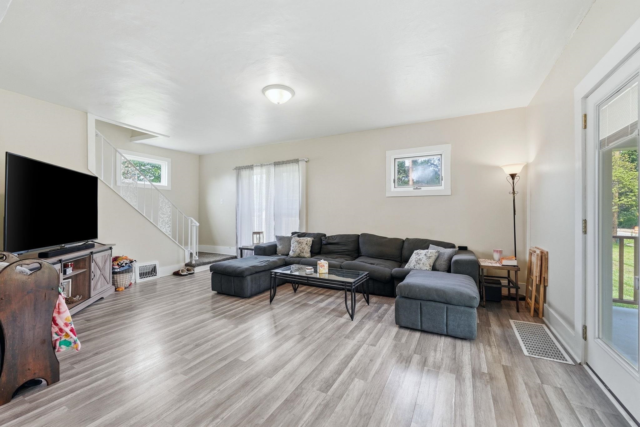 Spacious living area featuring wood-finish flooring, neutral wall tones, and a staircase with white railings