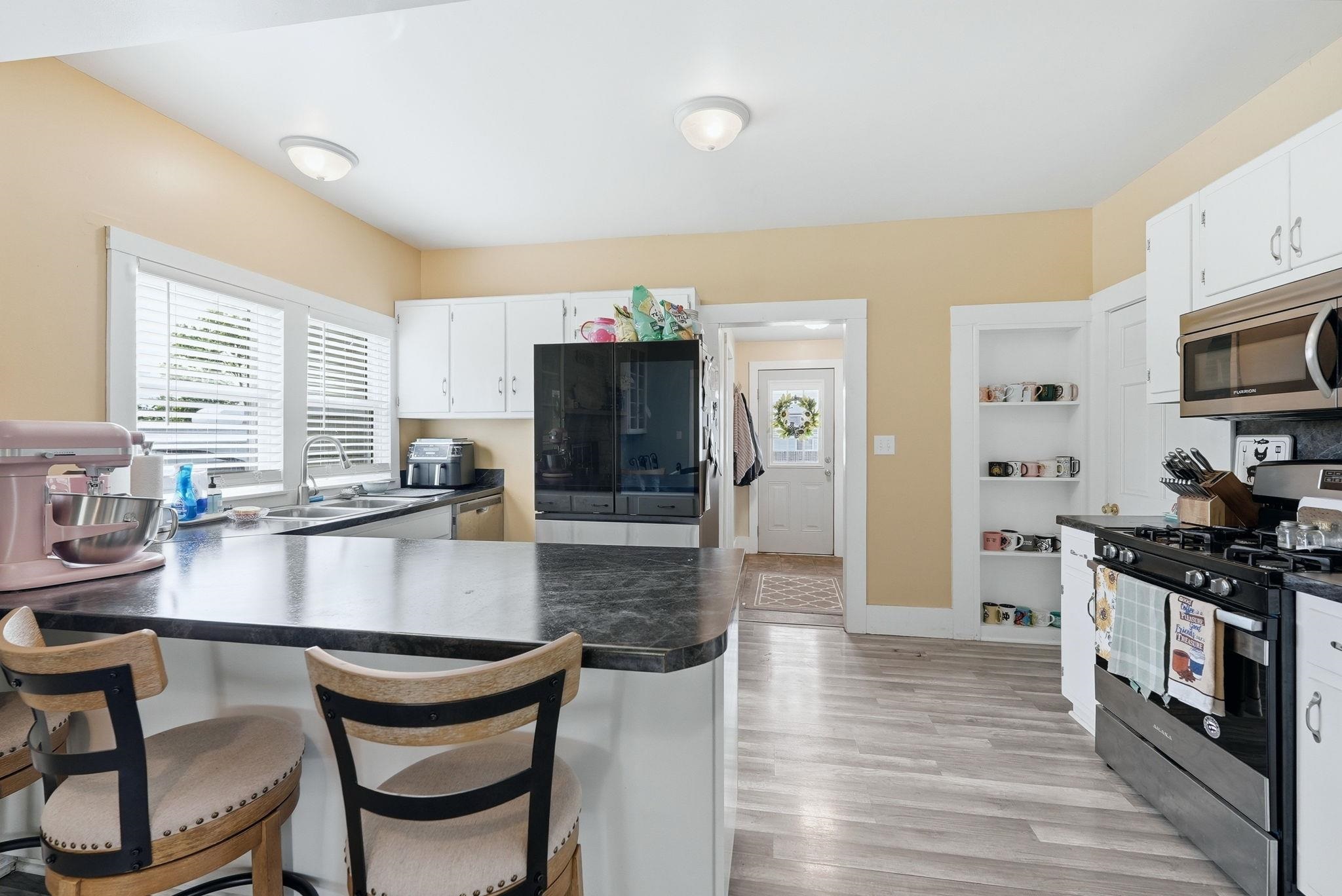 Kitchen featuring an eat-at island with a dark countertop, white cabinetry, wood-finish flooring, a stainless steel over-the-range microwave, and a gas range