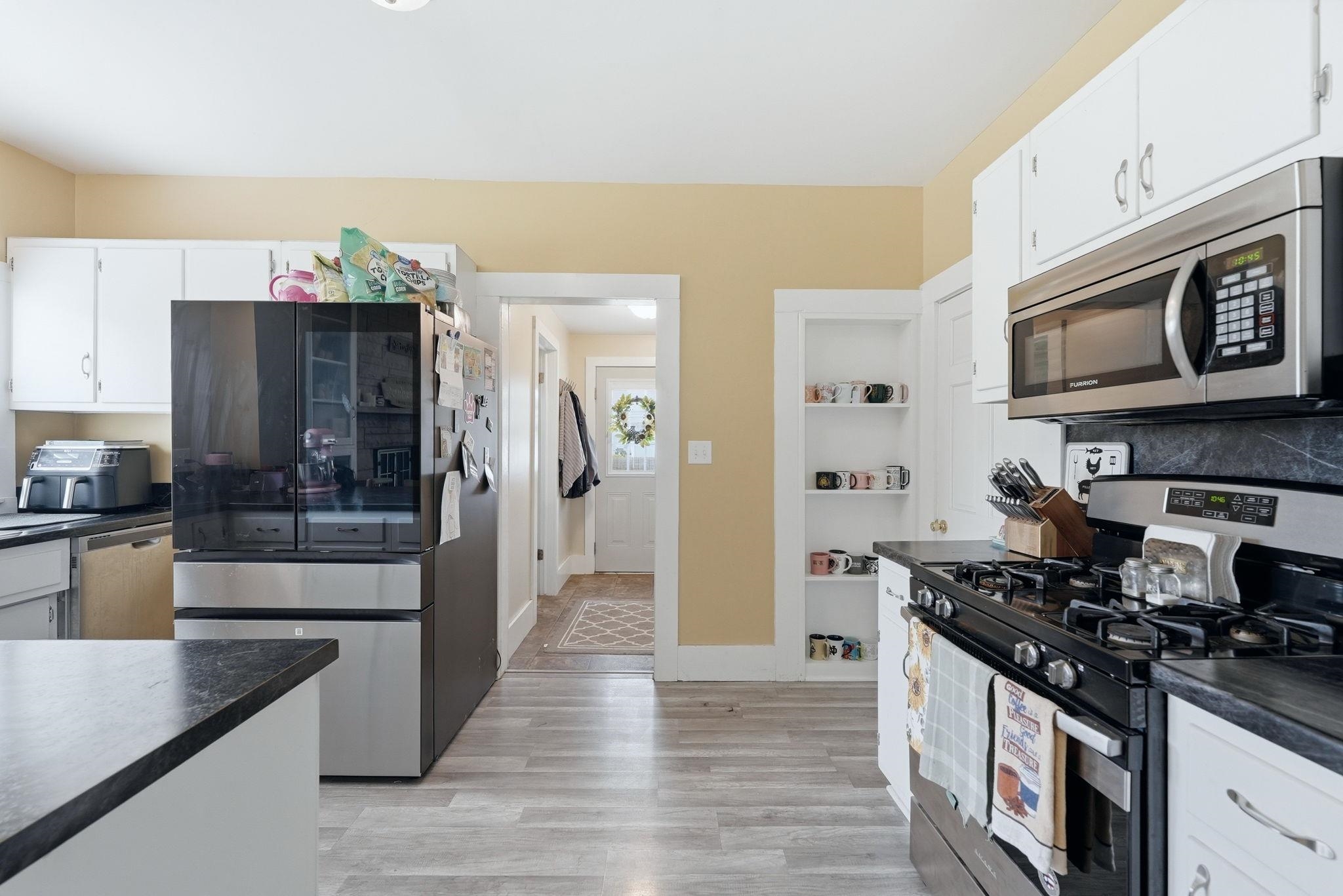 Kitchen featuring wood-finish flooring, white cabinetry, dark countertops, a built-in stainless steel microwave, and a gas range
