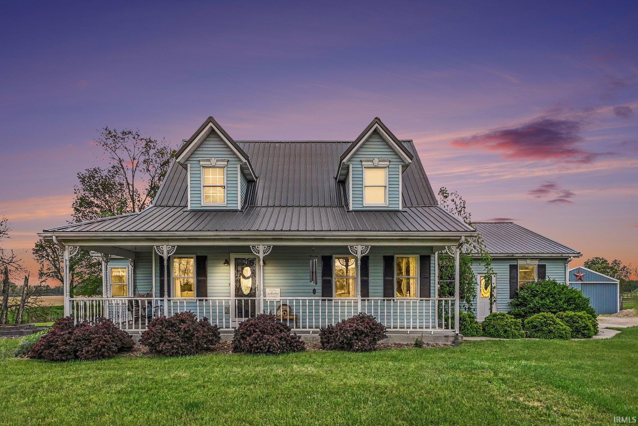 Light blue siding exterior with a dark metal roof, featuring a covered front porch with white railing