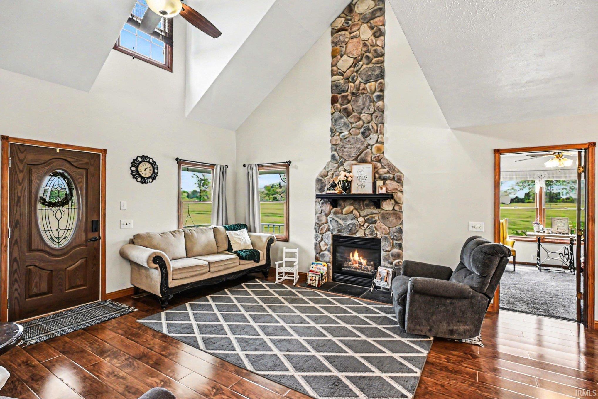 Vaulted ceiling living area featuring a prominent floor-to-ceiling stone fireplace, wood-finish flooring, and a decorative front entry door with an oval glass insert