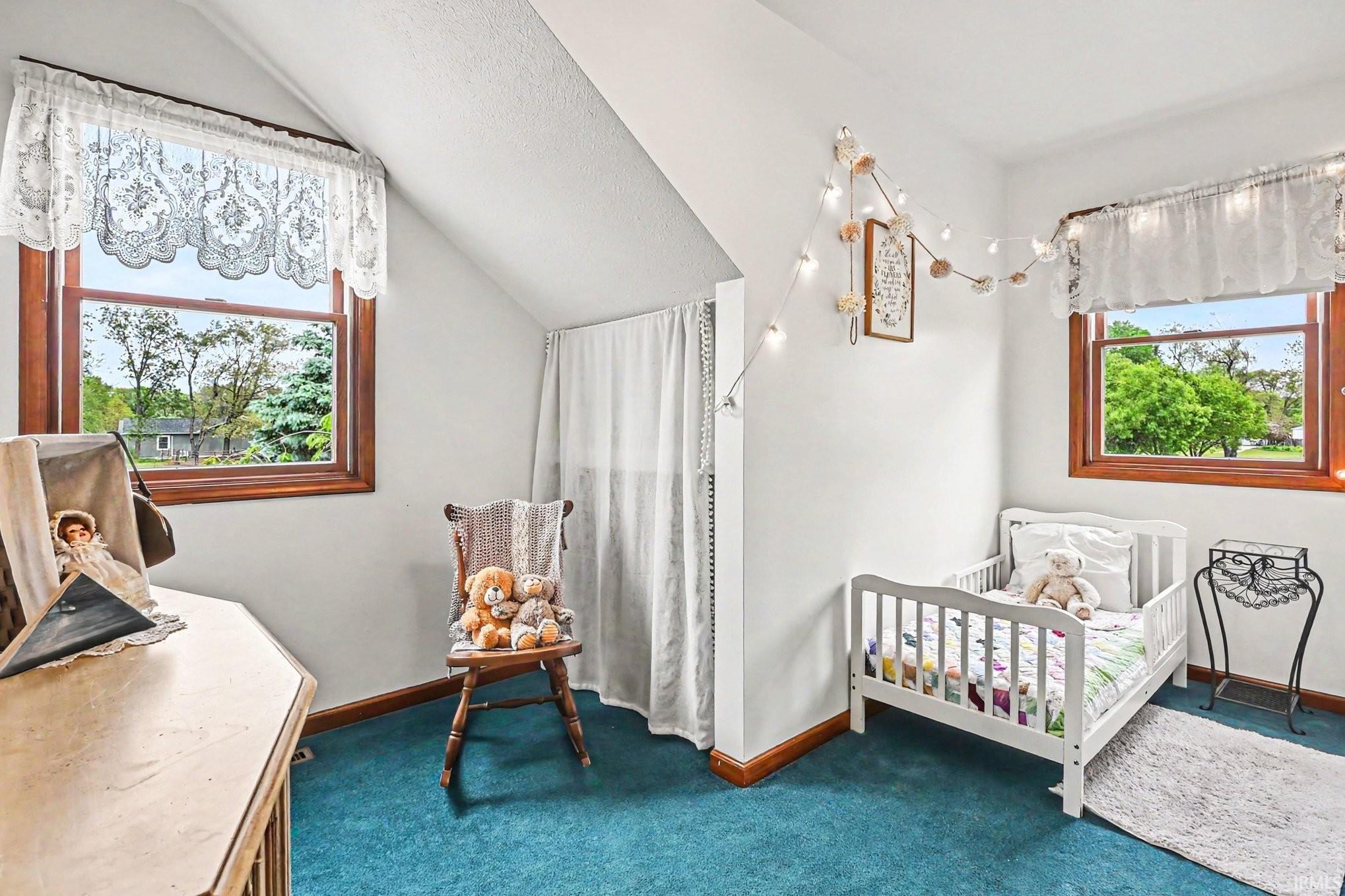 Bedroom featuring sloped ceilings, two wooden-framed windows, and blue carpeting