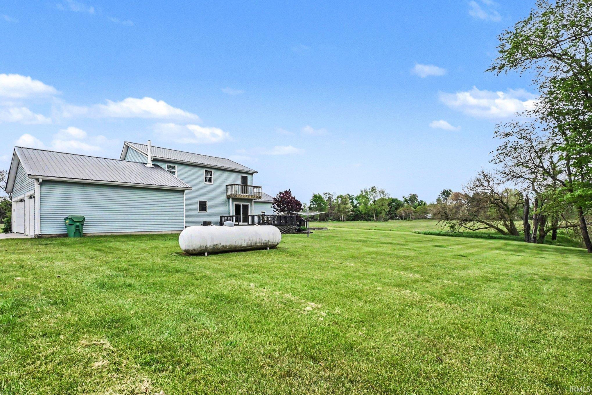 Expansive green lawn bordering a two-story residence with light blue siding and a gray metal roof