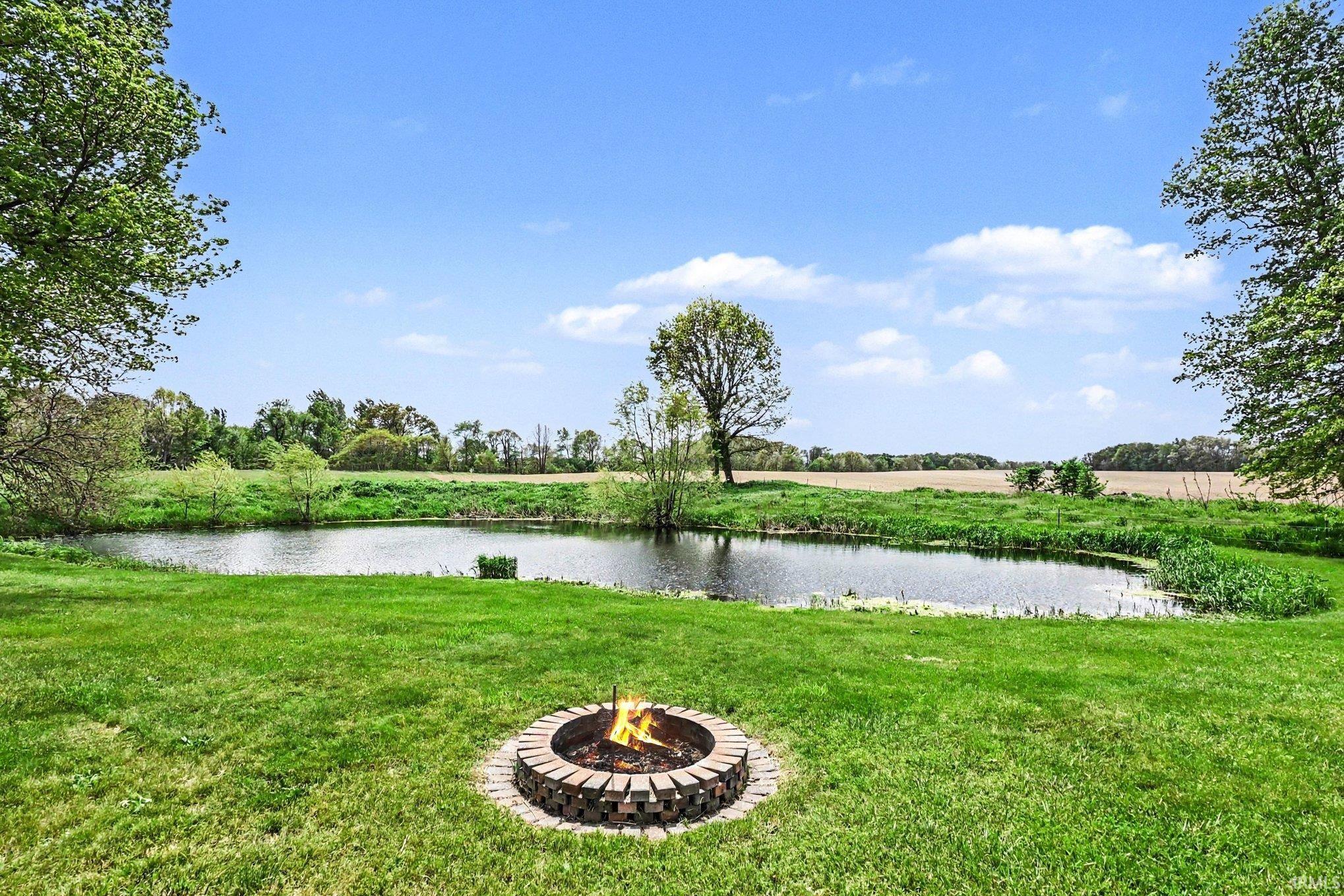 Expansive green lawn with a built-in stone fire pit, bordered by a tranquil pond