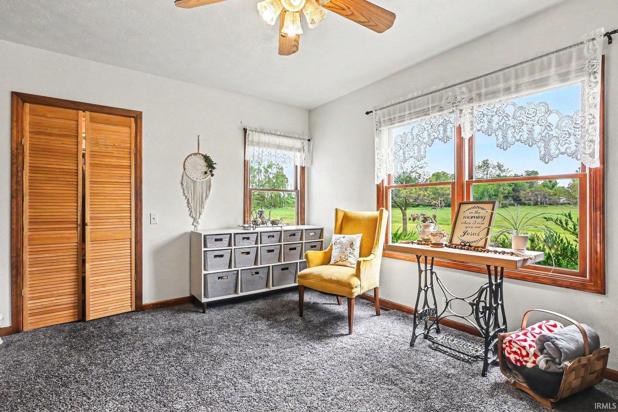Room featuring light-colored walls, wood-framed windows, dark gray carpeting, and a wood louvered bifold closet door