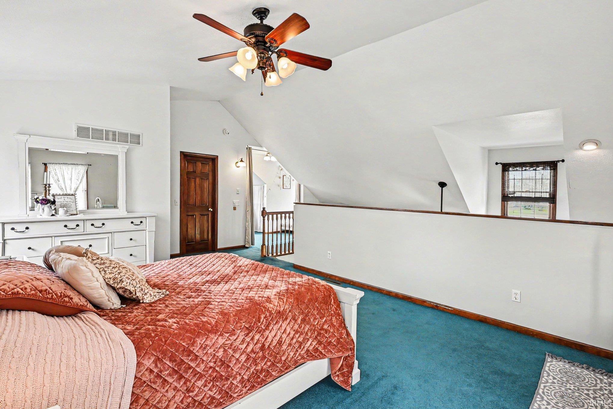 Spacious loft bedroom featuring angled ceilings, recessed lighting, a ceiling fan, and a wood-paneled door