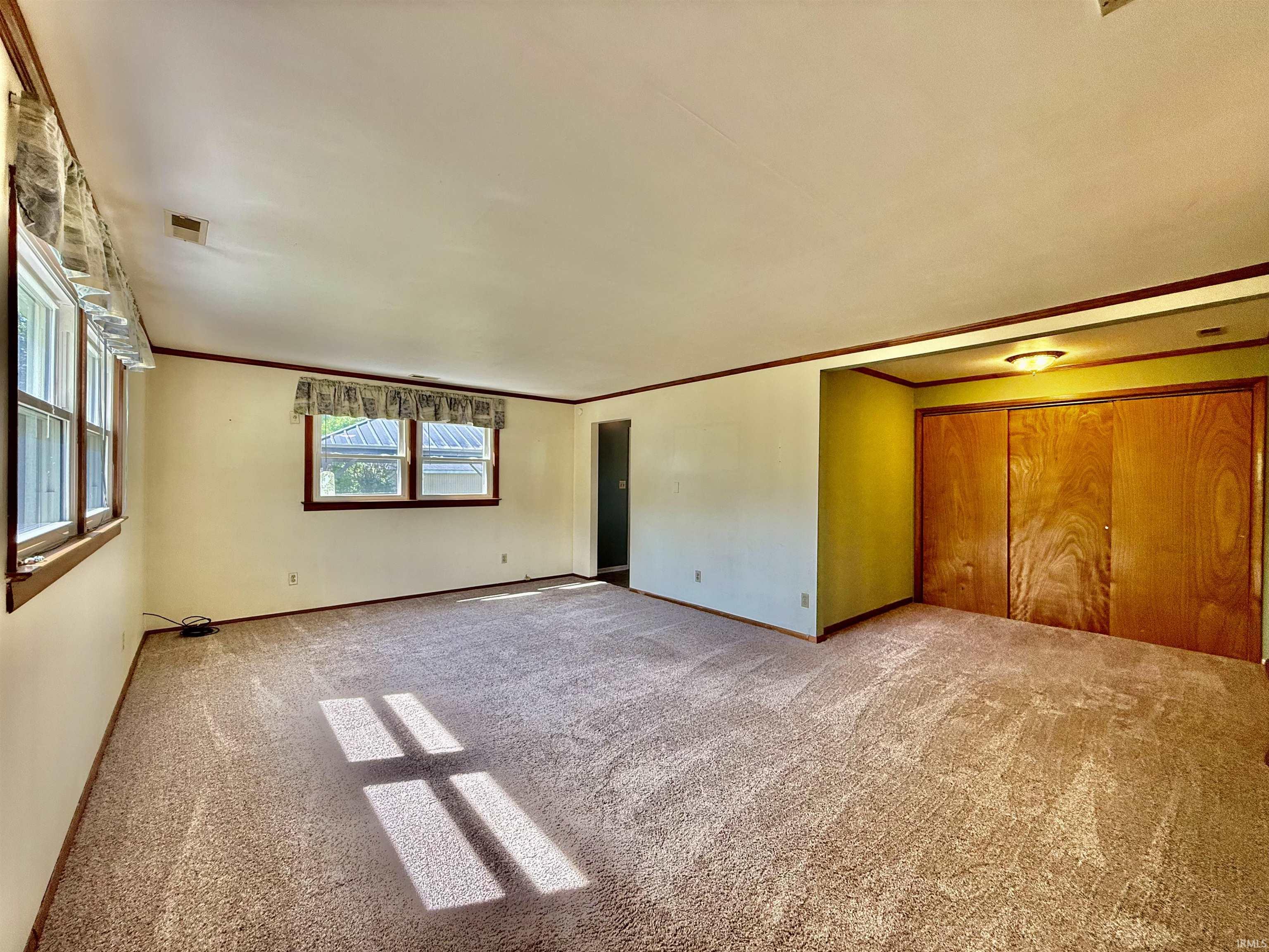 Spacious room featuring neutral carpet flooring, multiple double-hung windows, wood-trim baseboards, and a built-in closet with wood-panel sliding doors