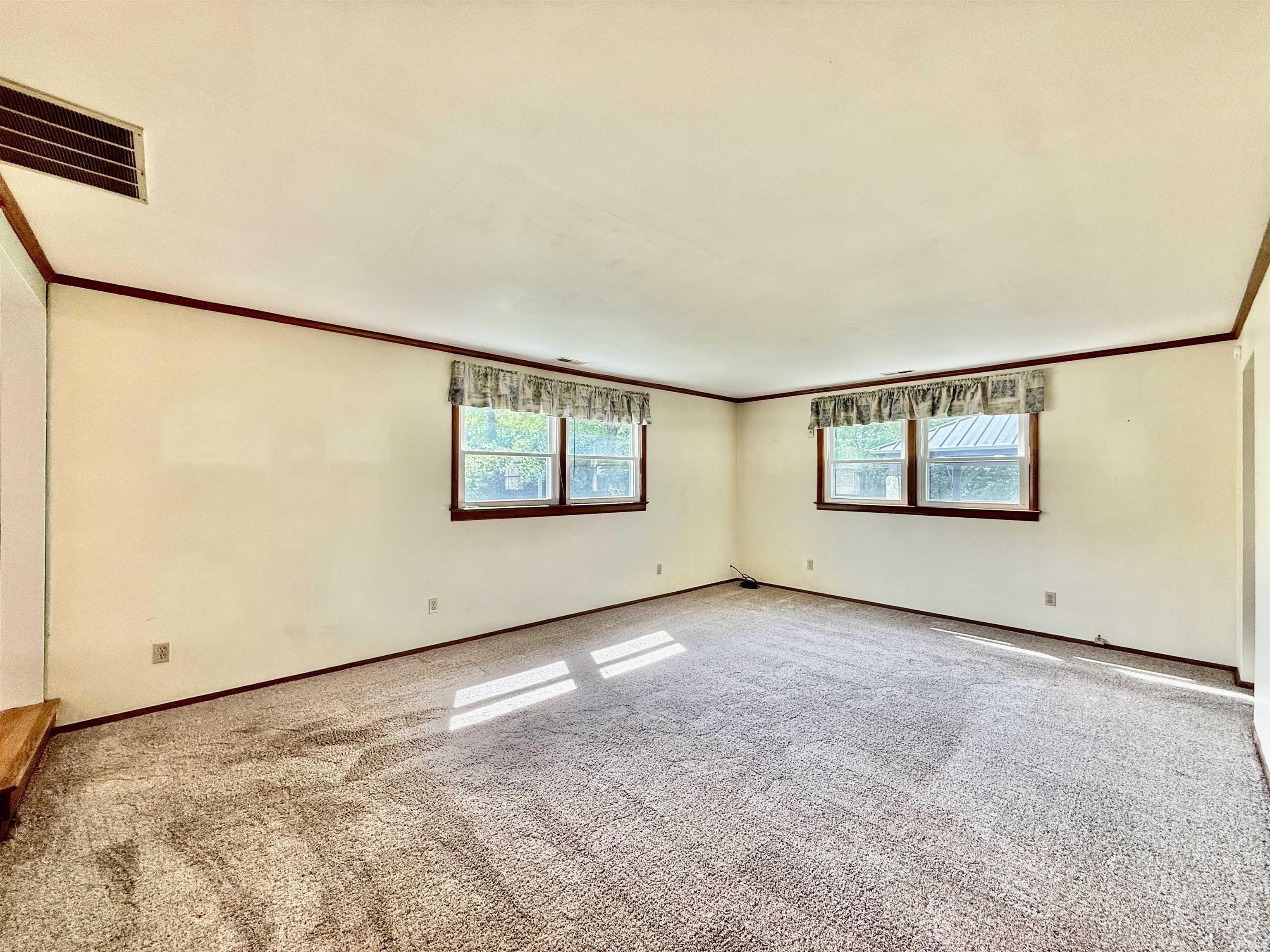 Spacious room featuring neutral carpet flooring, light-toned walls, and dark wood trim