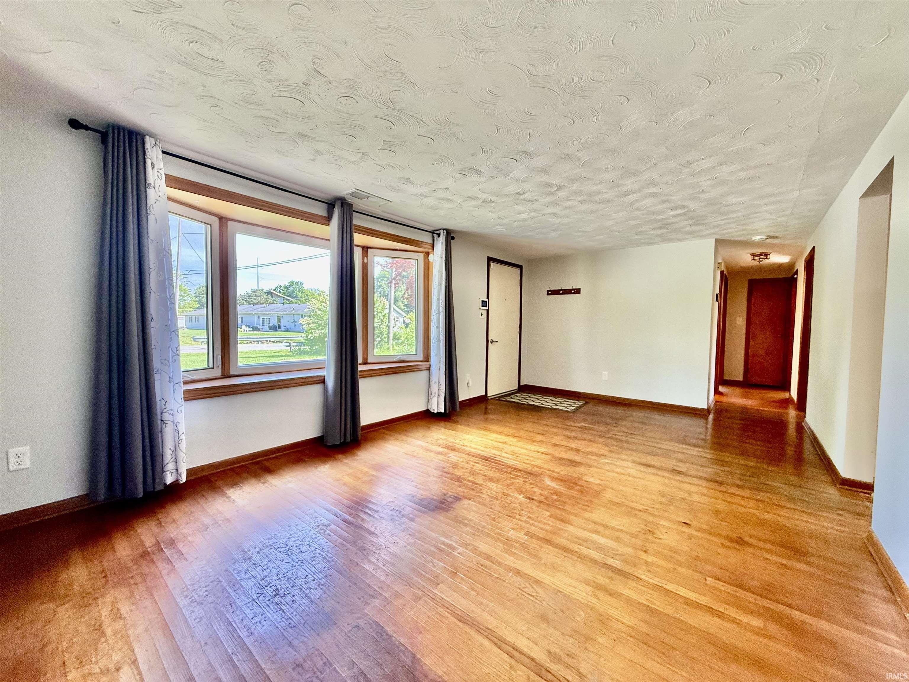 Spacious living area featuring wood-finish flooring, a prominent bay window with wood trim, and neutral wall tones
