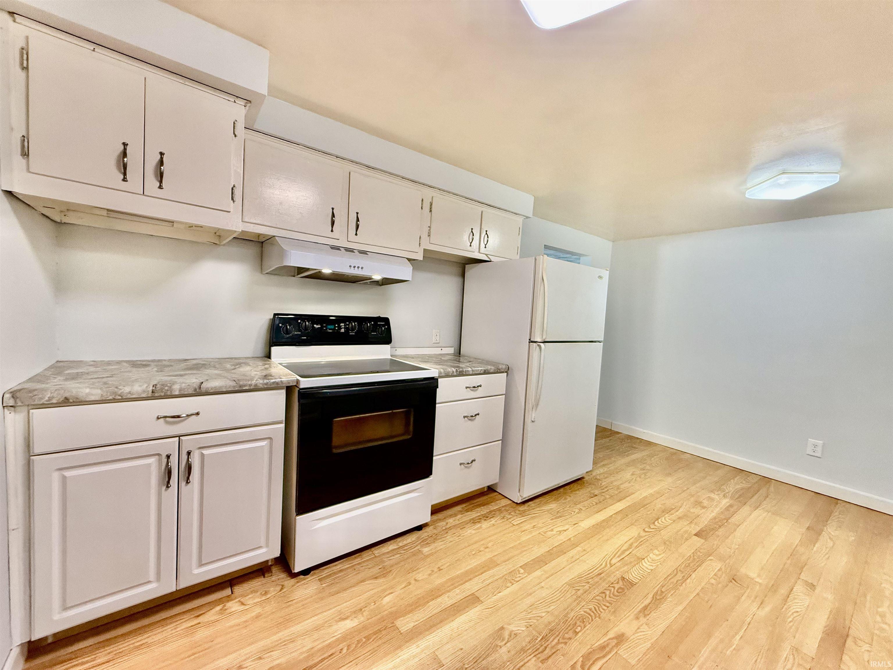 Kitchen area featuring wood-finish flooring, white cabinetry with dark hardware, and a built-in range