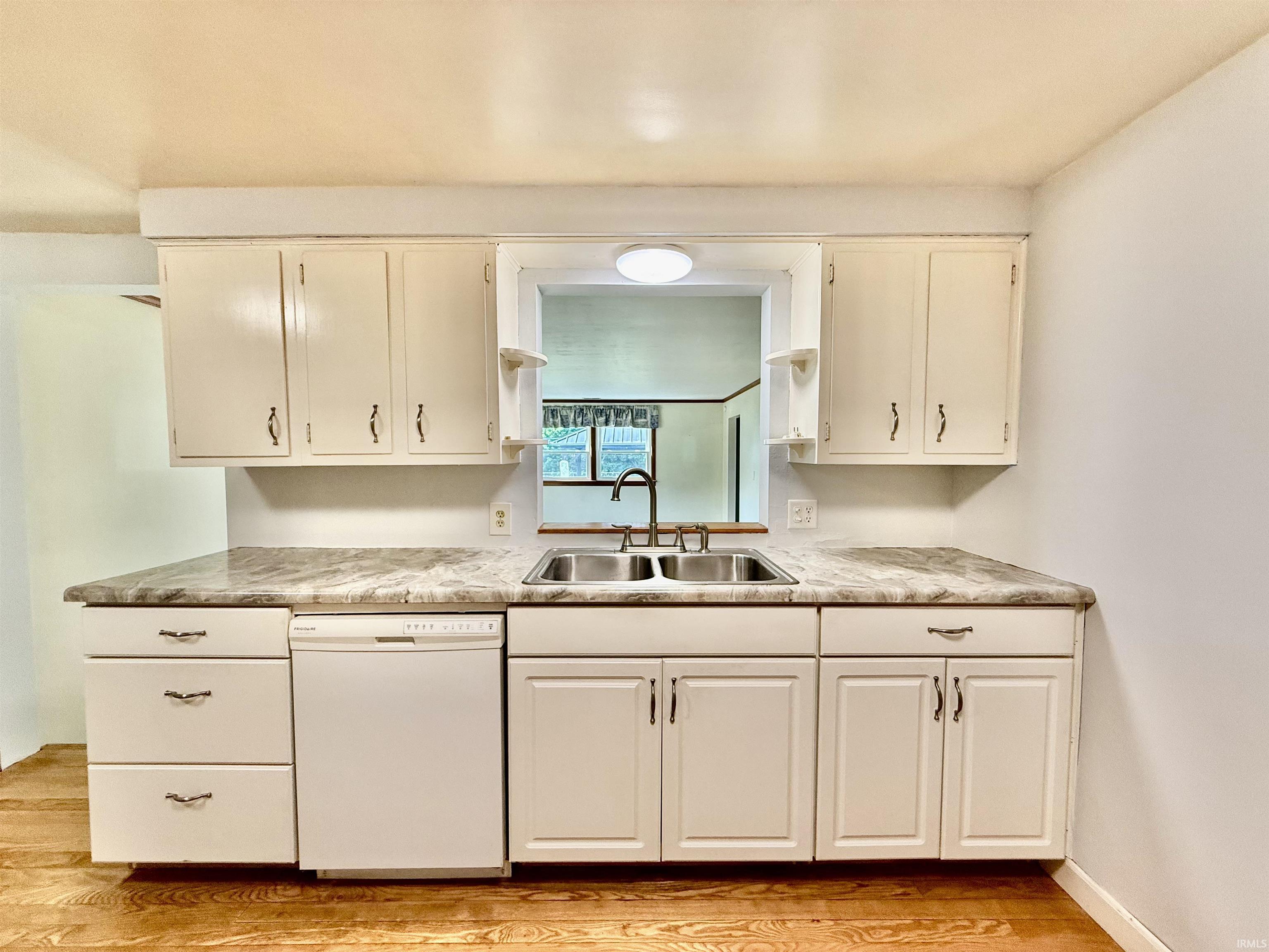 Kitchen featuring wood-finish flooring, white cabinetry, a double basin stainless steel sink with a gooseneck faucet, light-toned countertops, and a built-in dishwasher