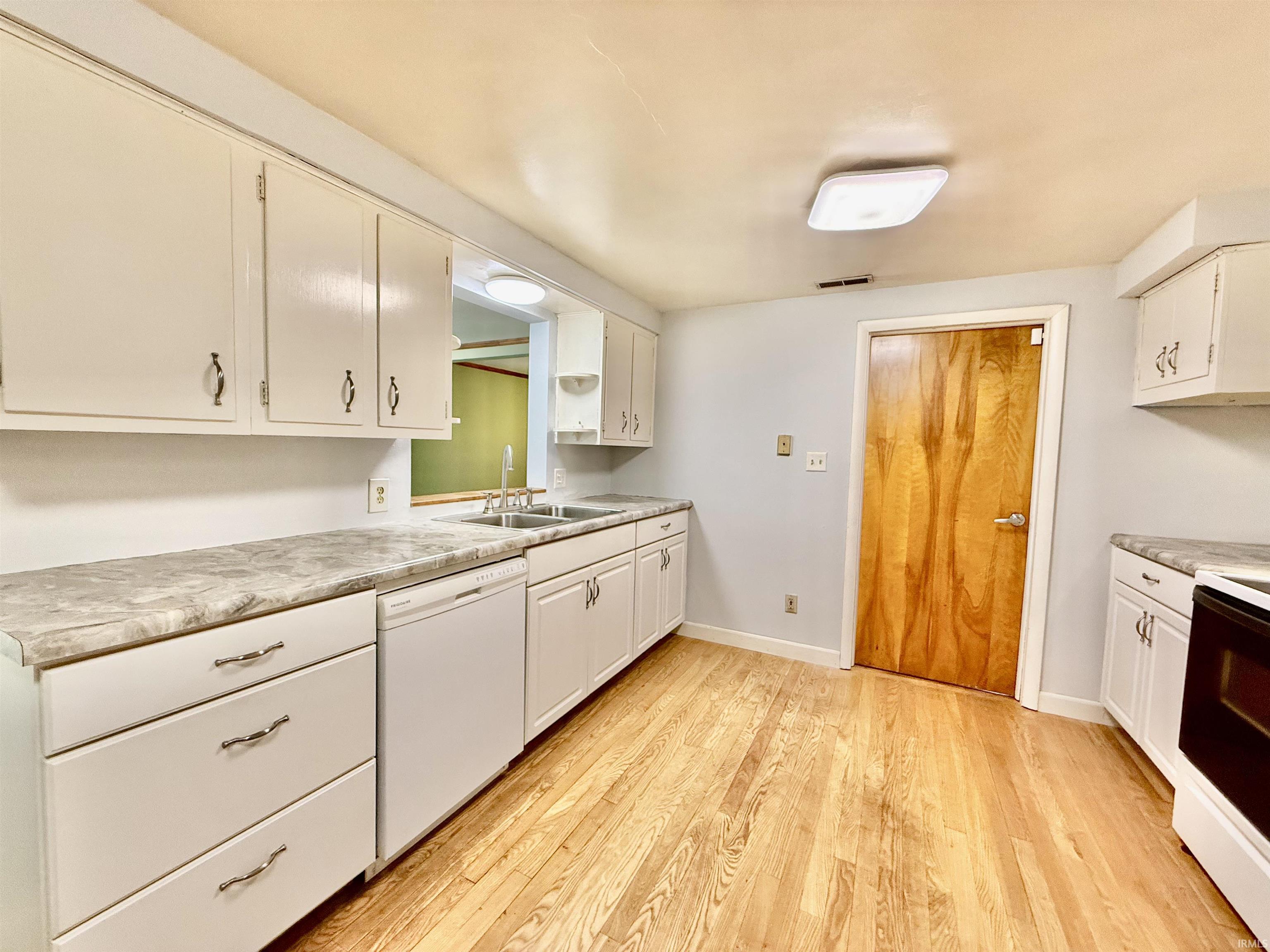 Kitchen featuring white cabinetry, light-toned wood-finish flooring, a double basin stainless steel sink, a white dishwasher, and light gray countertops