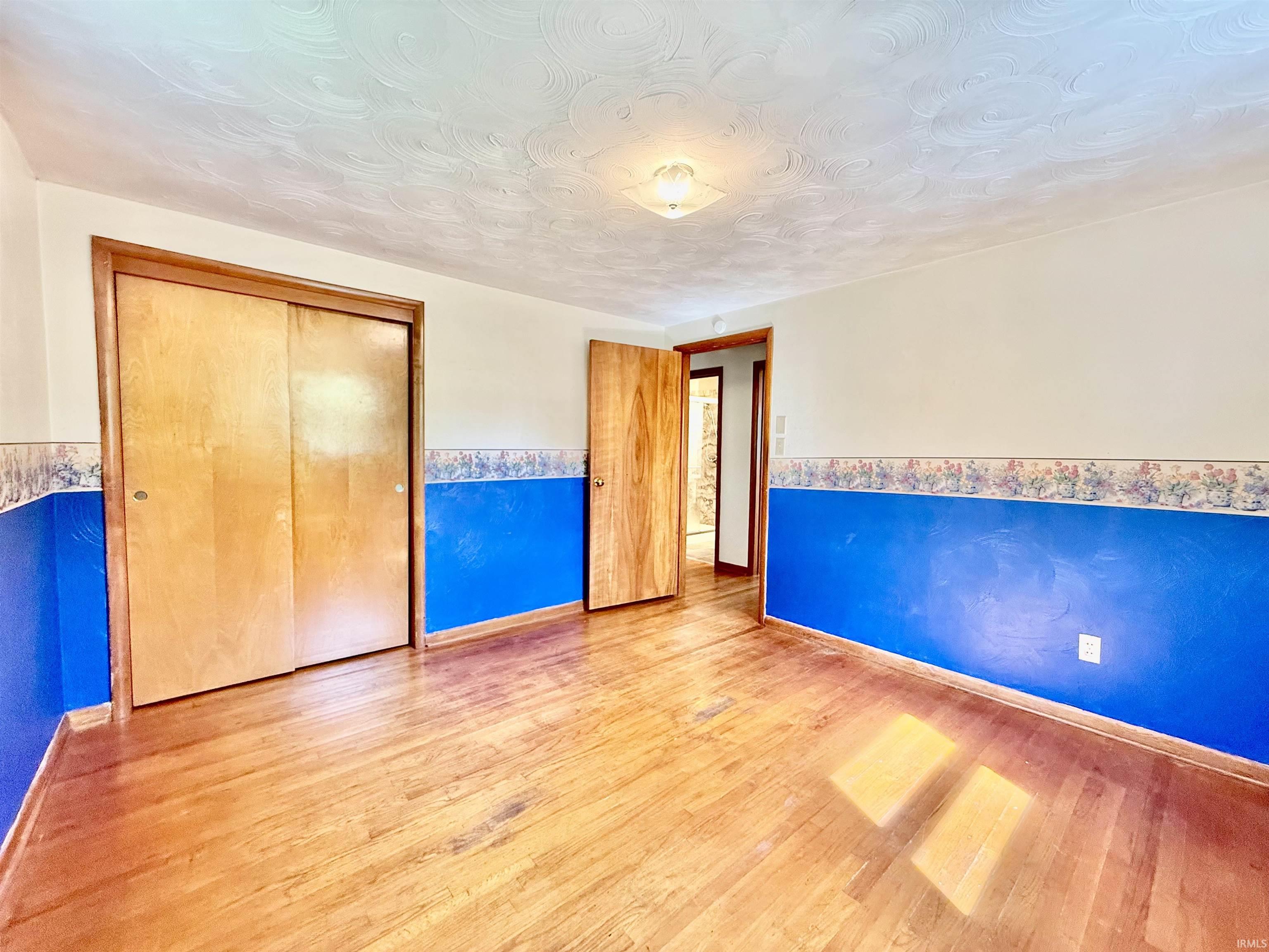Interior room featuring wood-finish flooring, a flush-mount ceiling light fixture, and a built-in closet with sliding wood doors
