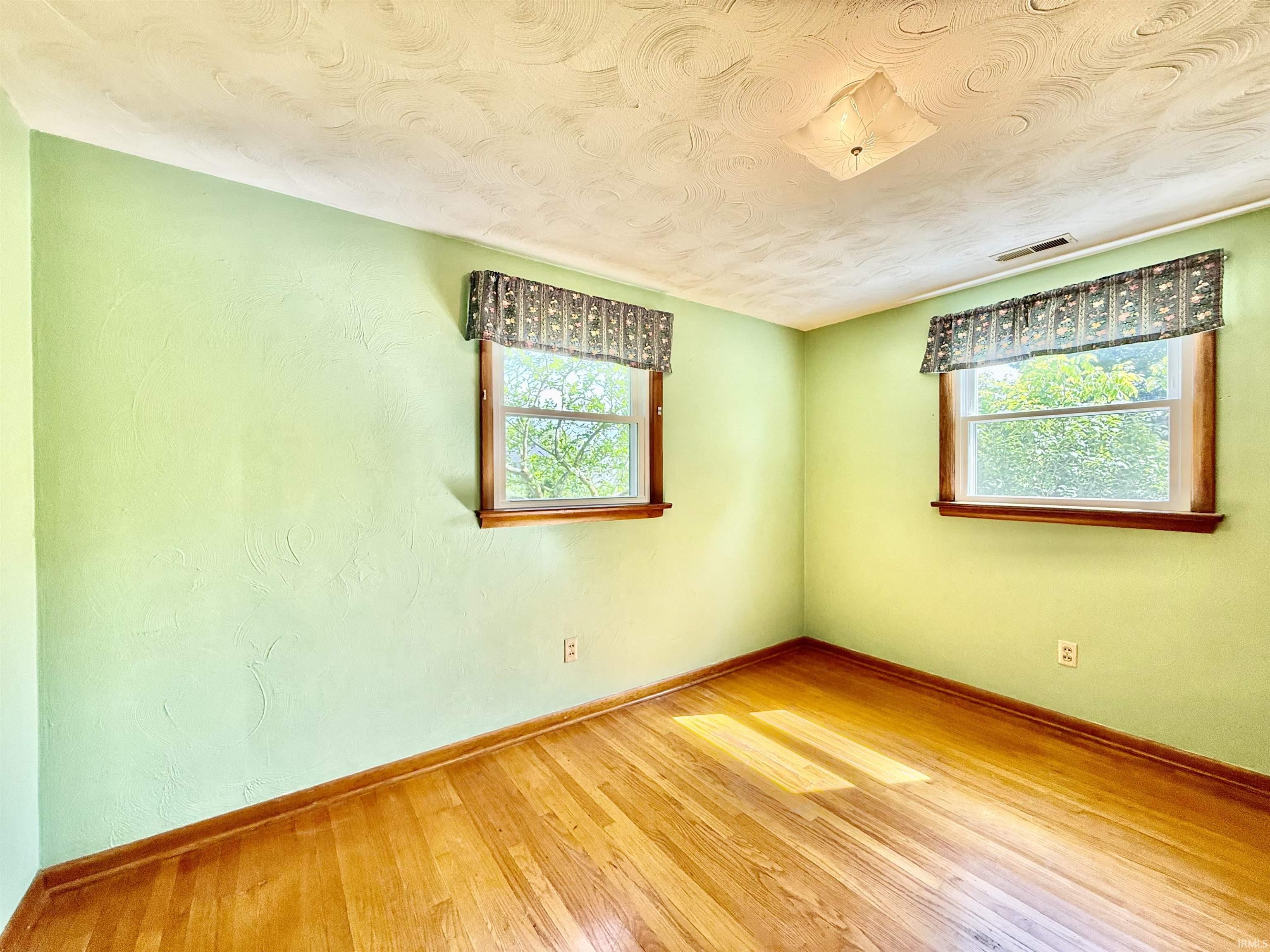 Room featuring wood-finish flooring, two windows with wood trim, and a ceiling-mounted light fixture