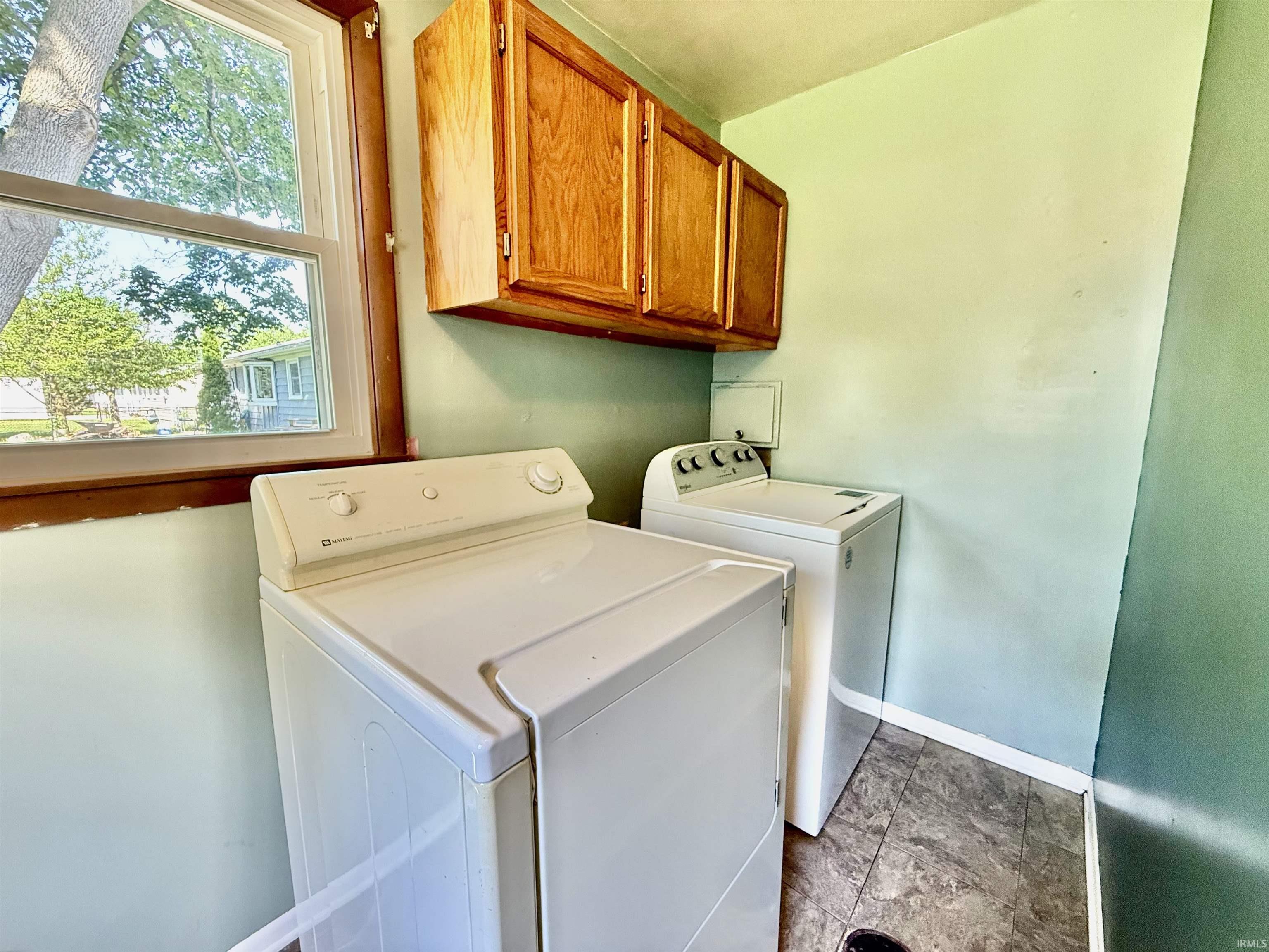 Utility space featuring wood-finish wall cabinets, a window with wood trim, and wood-finish flooring