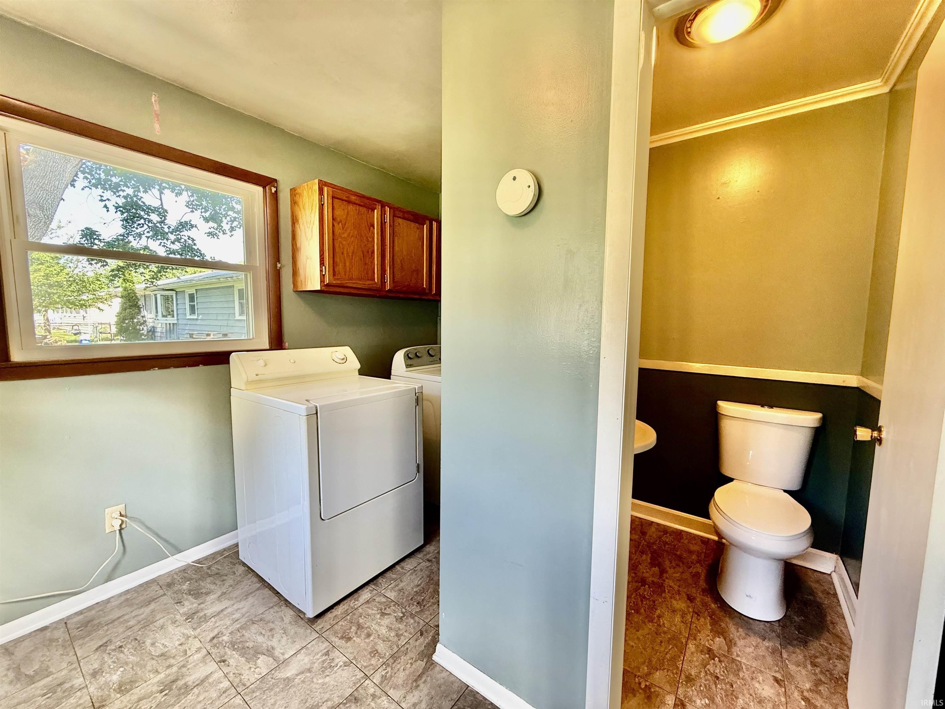Laundry area with wood-finish wall cabinets, a window with wood trim, and resilient flooring