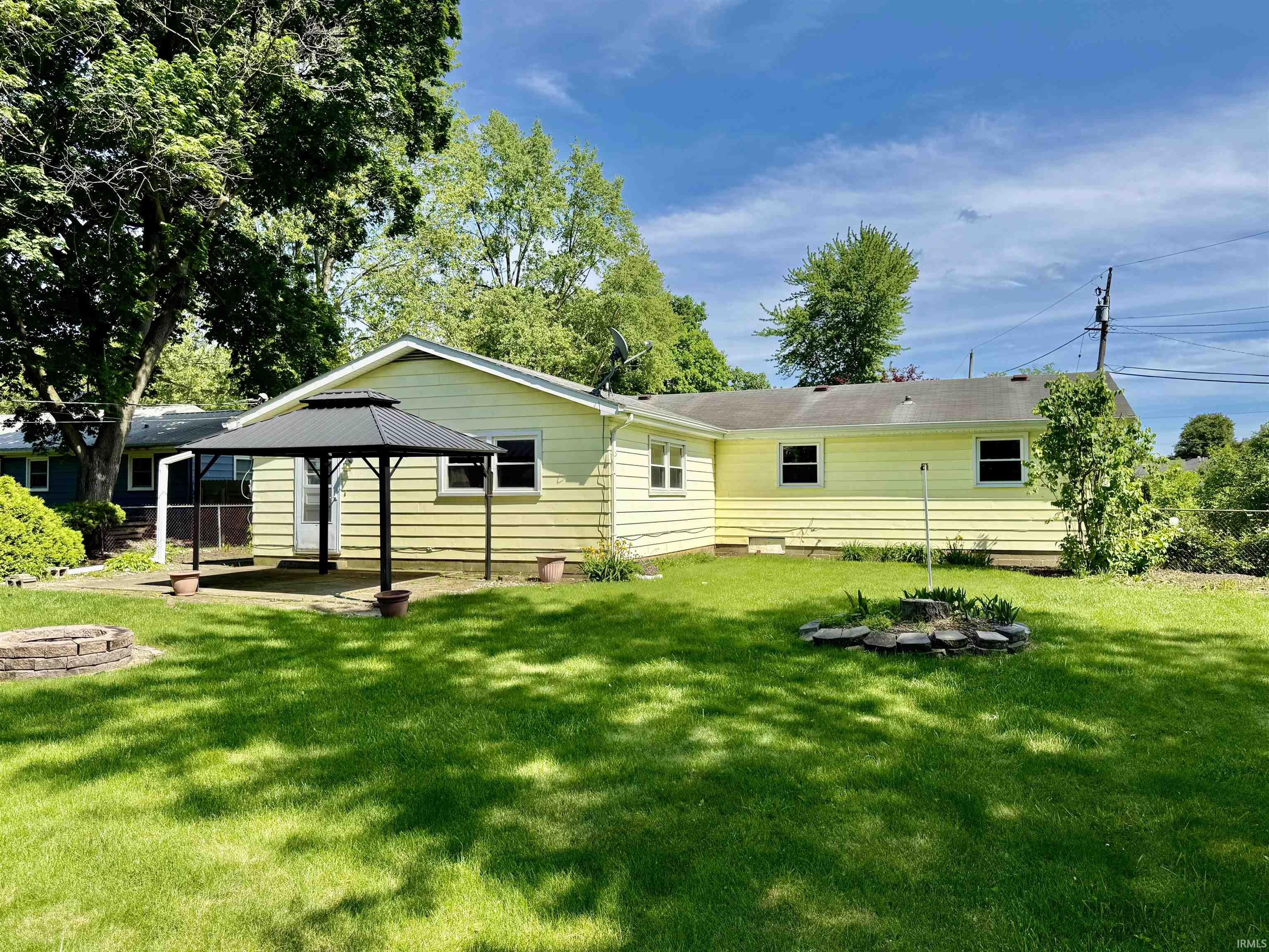 Expansive backyard featuring a manicured lawn, a paved patio, and a standalone gazebo with a tiered roof