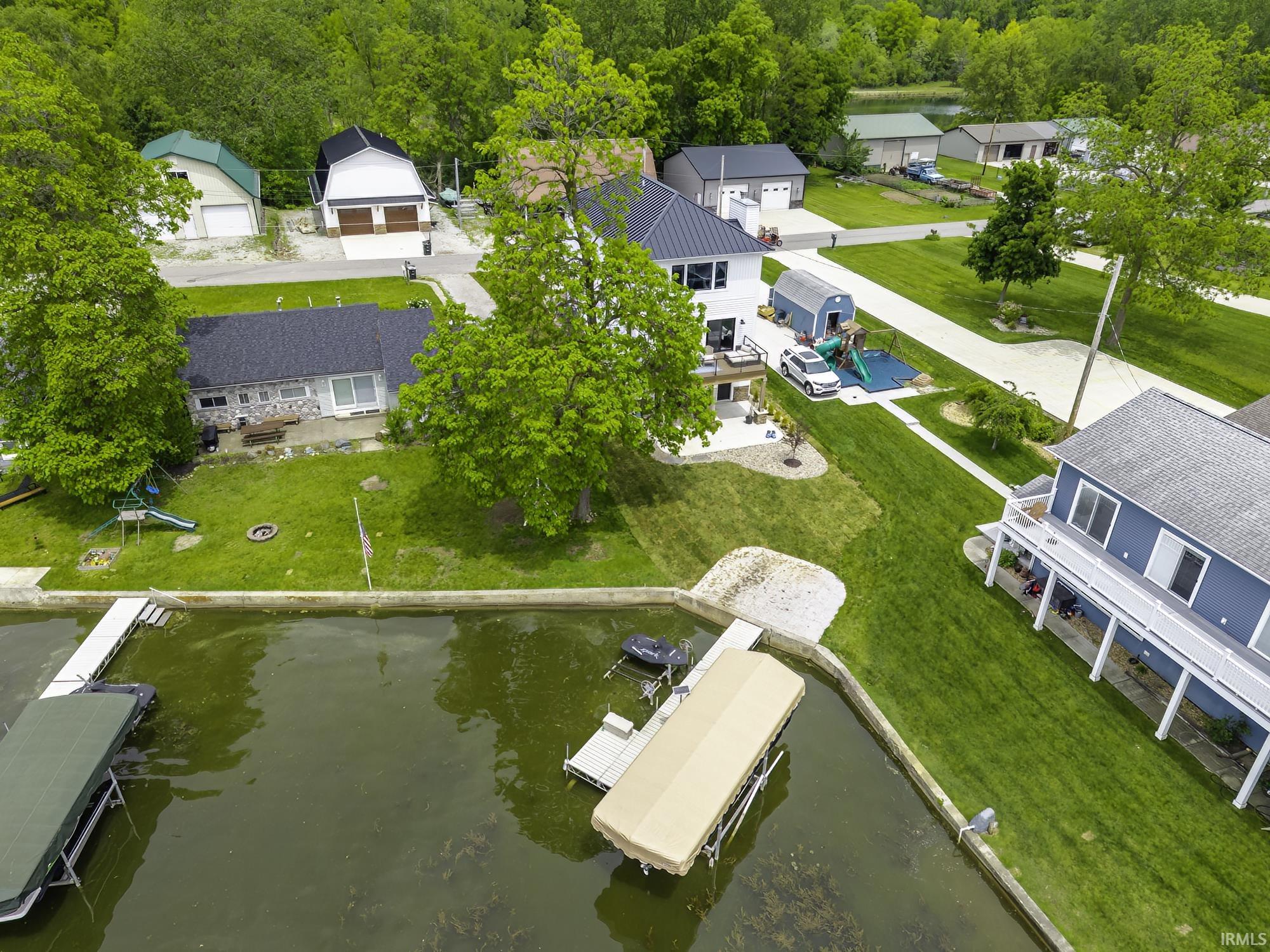 Waterfront property featuring a private boat dock, green lawn, mature trees, and an additional detached garage structure