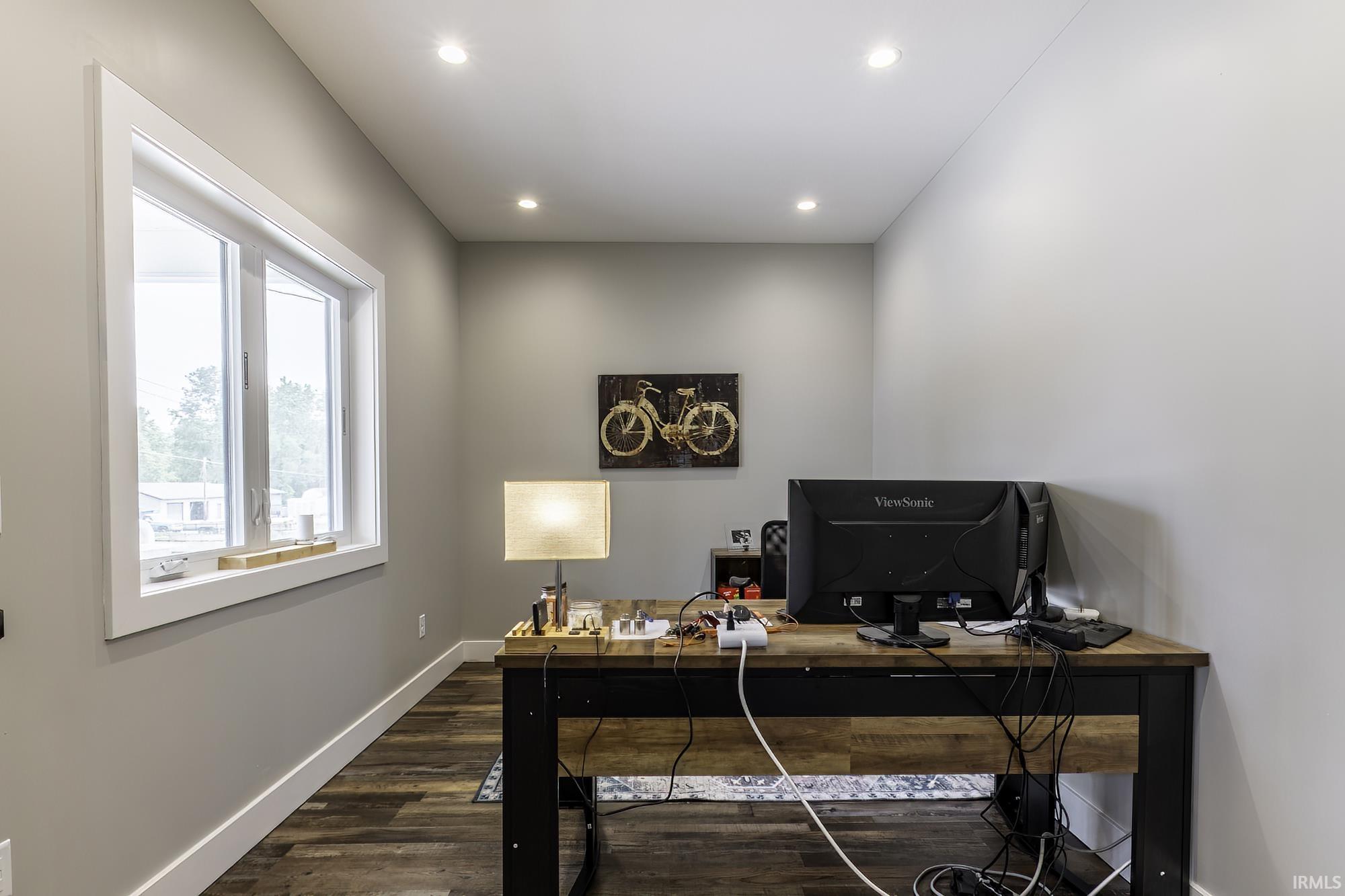 Neutral-toned room featuring a large window with white trim, recessed ceiling lighting, and wood-finish flooring