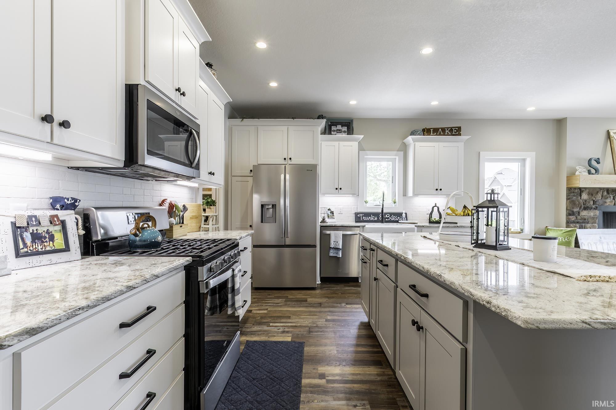 Kitchen featuring white cabinetry, stainless steel appliances, granite countertops, a subway tile backsplash, and wood-finish flooring