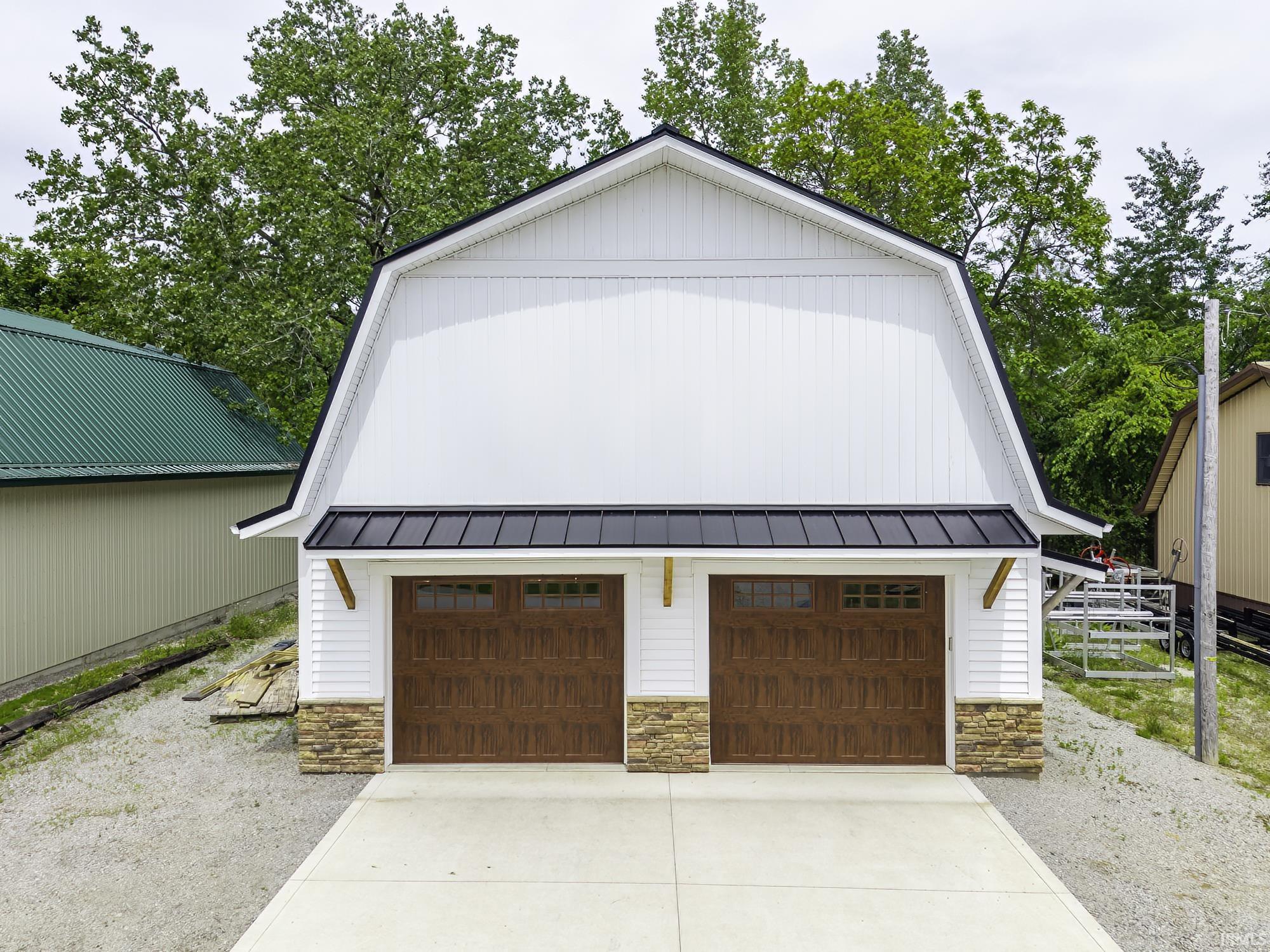 Two-car garage featuring a gambrel roof and white vertical siding