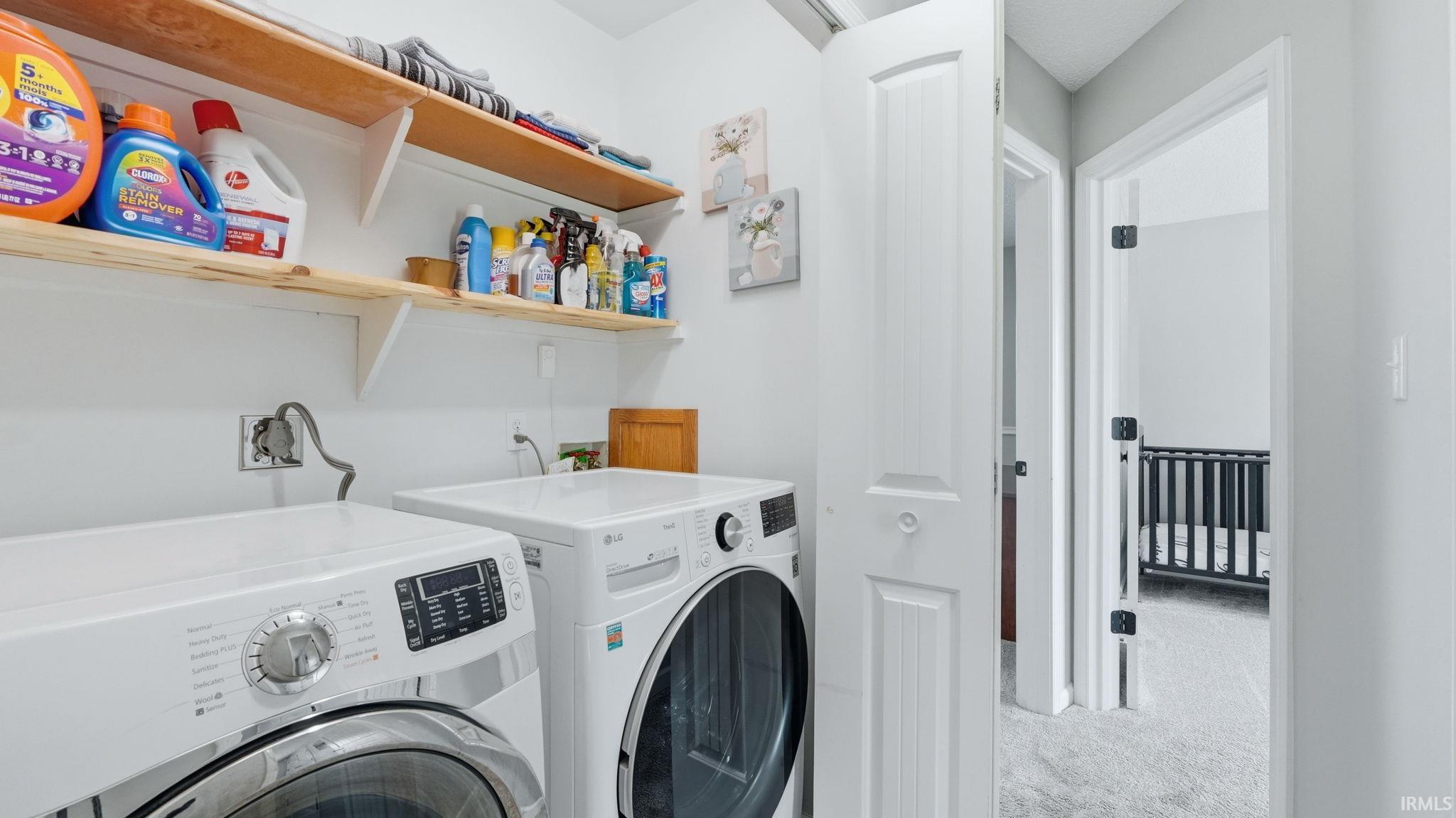 Dedicated laundry area featuring a white front-loading washer and dryer, two wood-finish wall-mounted shelves, and white painted walls