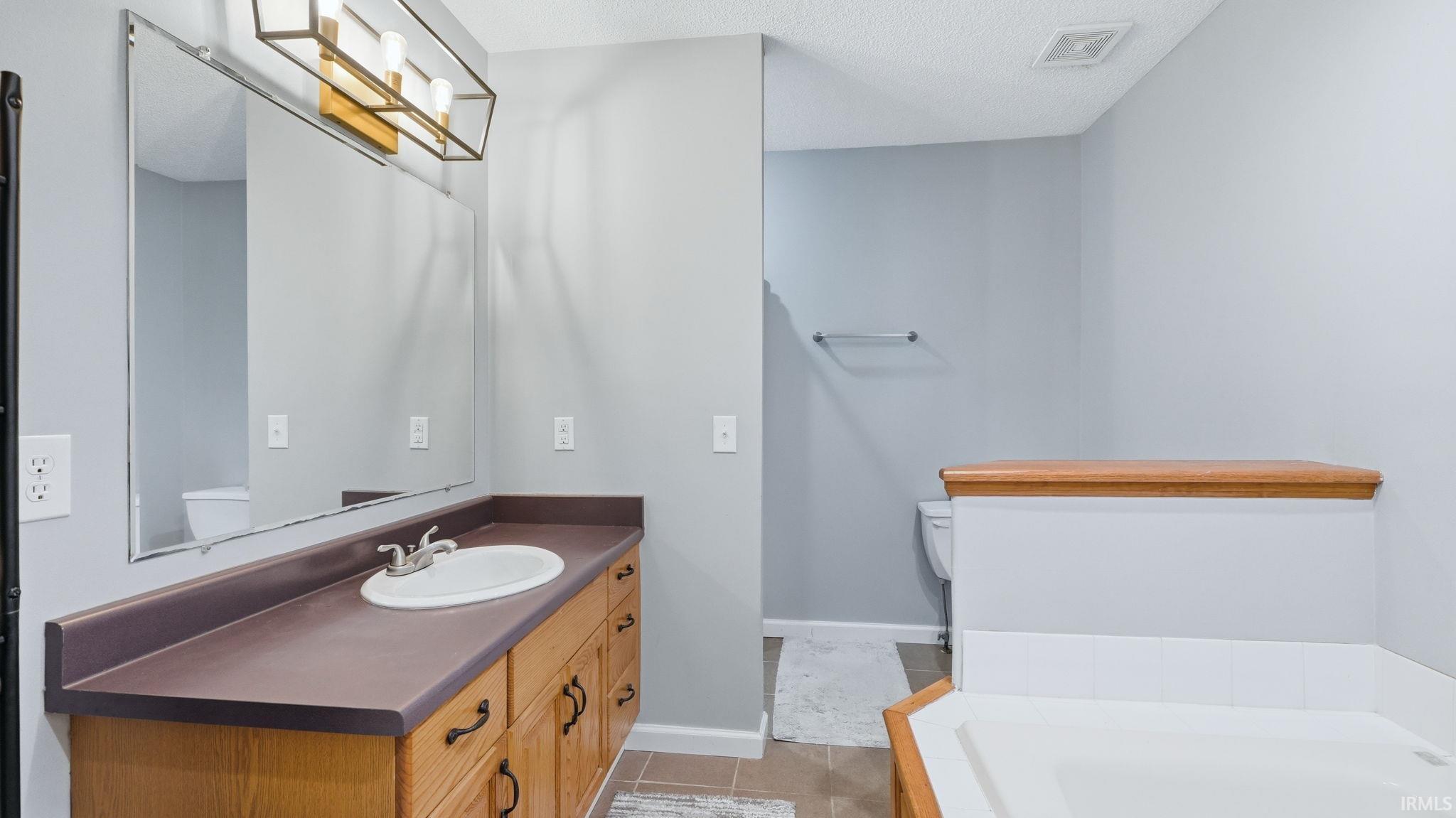 Bathroom featuring a wood-finish vanity with an integrated sink and dark countertop, a large wall-mounted mirror, and a modern light fixture with three exposed bulbs
