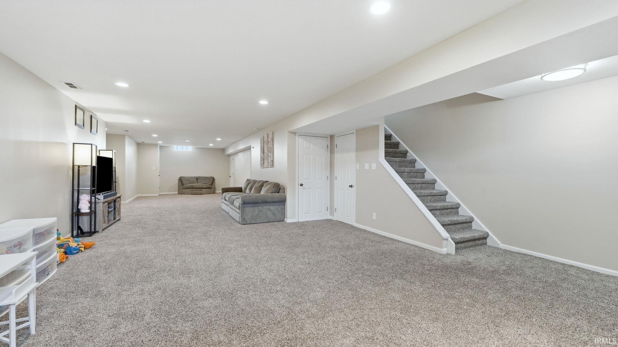 Expansive finished lower level featuring neutral carpeting, recessed lighting, and a painted staircase