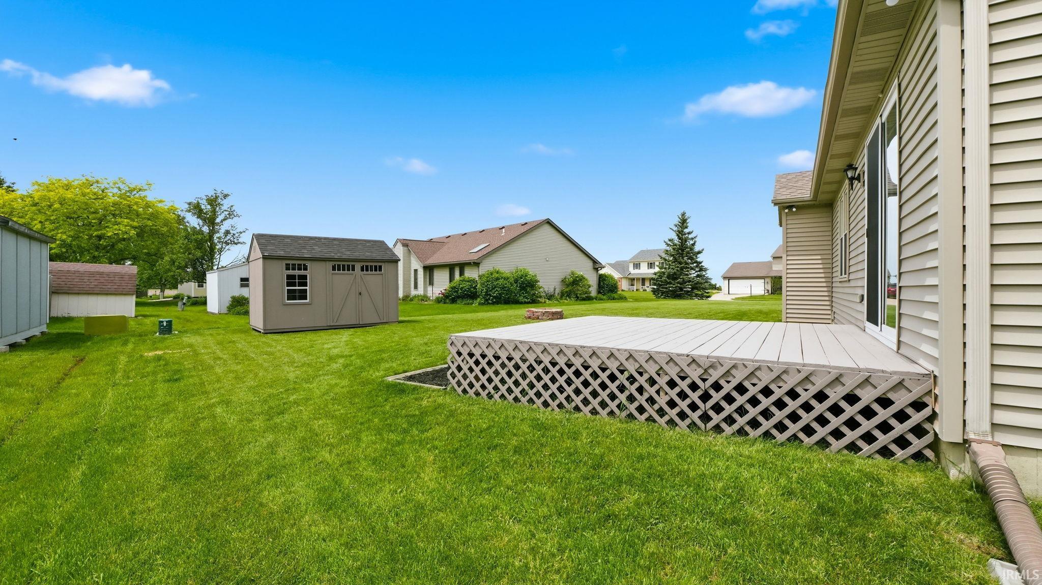 Expansive backyard featuring a large outdoor deck with lattice skirting, a detached storage shed with a shingled roof, a sliding glass door entry to the residence, and vinyl siding exterior