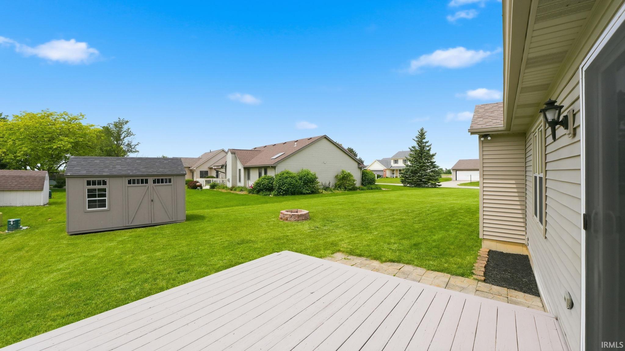 Expansive backyard featuring a light-colored wood-finish deck, a tan storage shed with a window, a fire pit, and mature landscaping