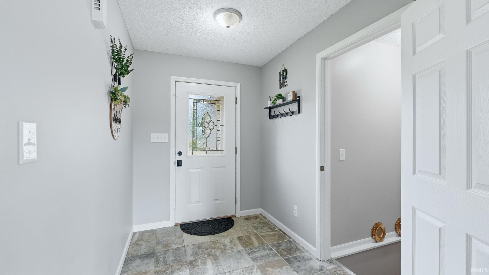 Entryway featuring durable tile flooring, a white paneled door with decorative glass inserts, light grey wall paint, white trim, and a semi-flush mount ceiling light fixture