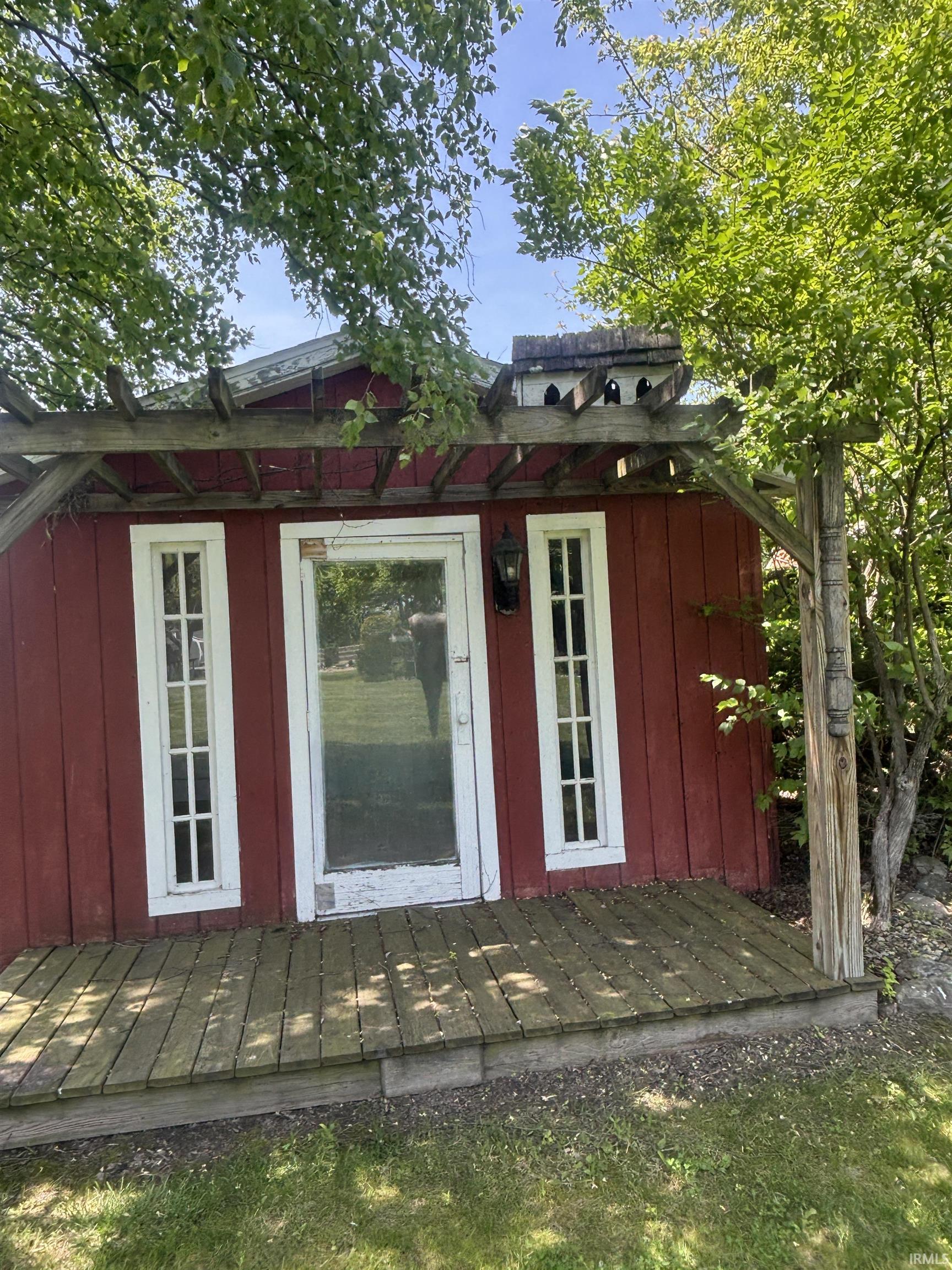 Red vertical siding structure featuring a front door with glass paneling, flanked by two multi-pane windows
