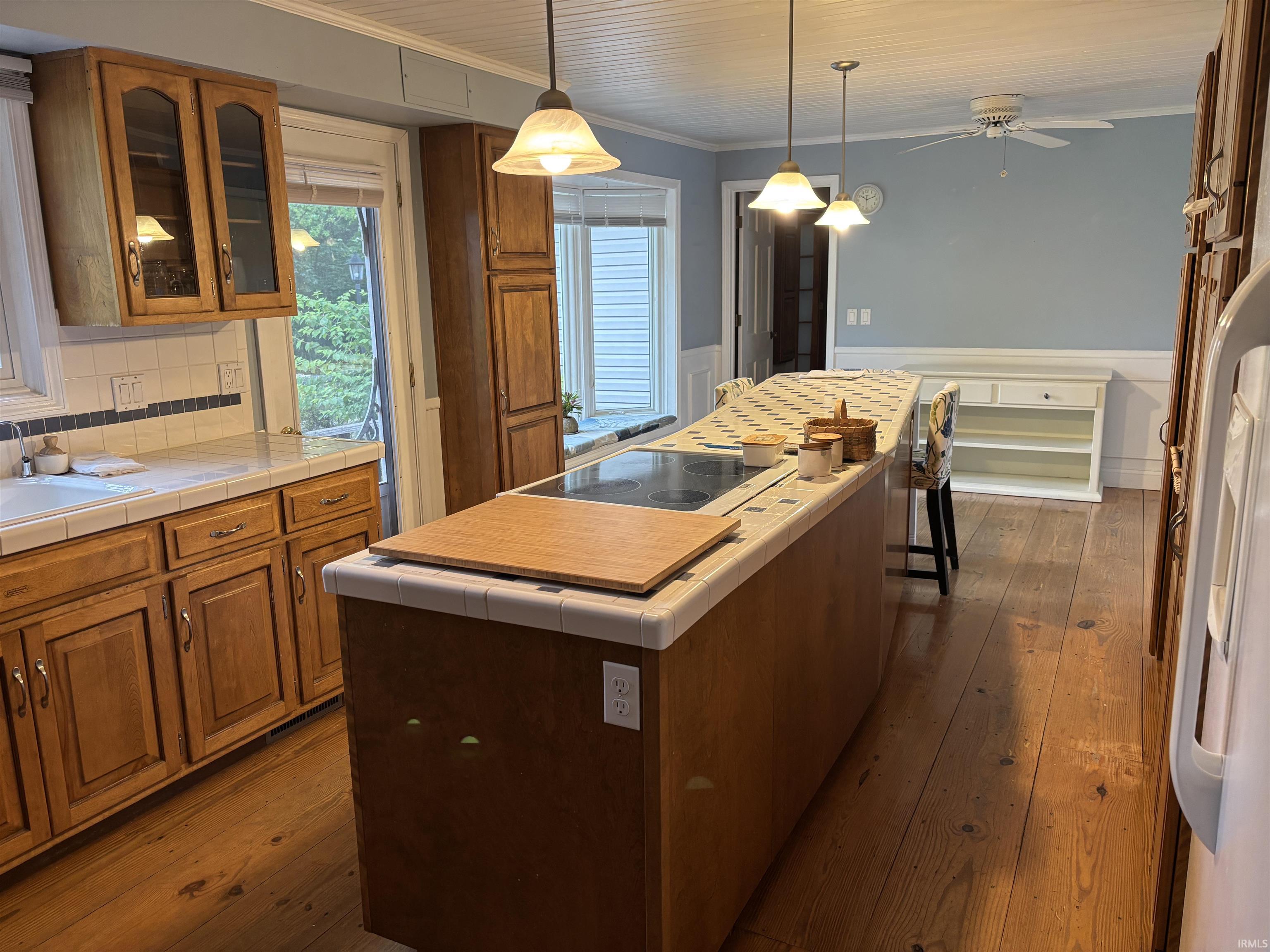 Kitchen featuring a large central island with integrated cooktop, wood-finish flooring, ample cabinetry, ceramic tile countertops, and wainscoting
