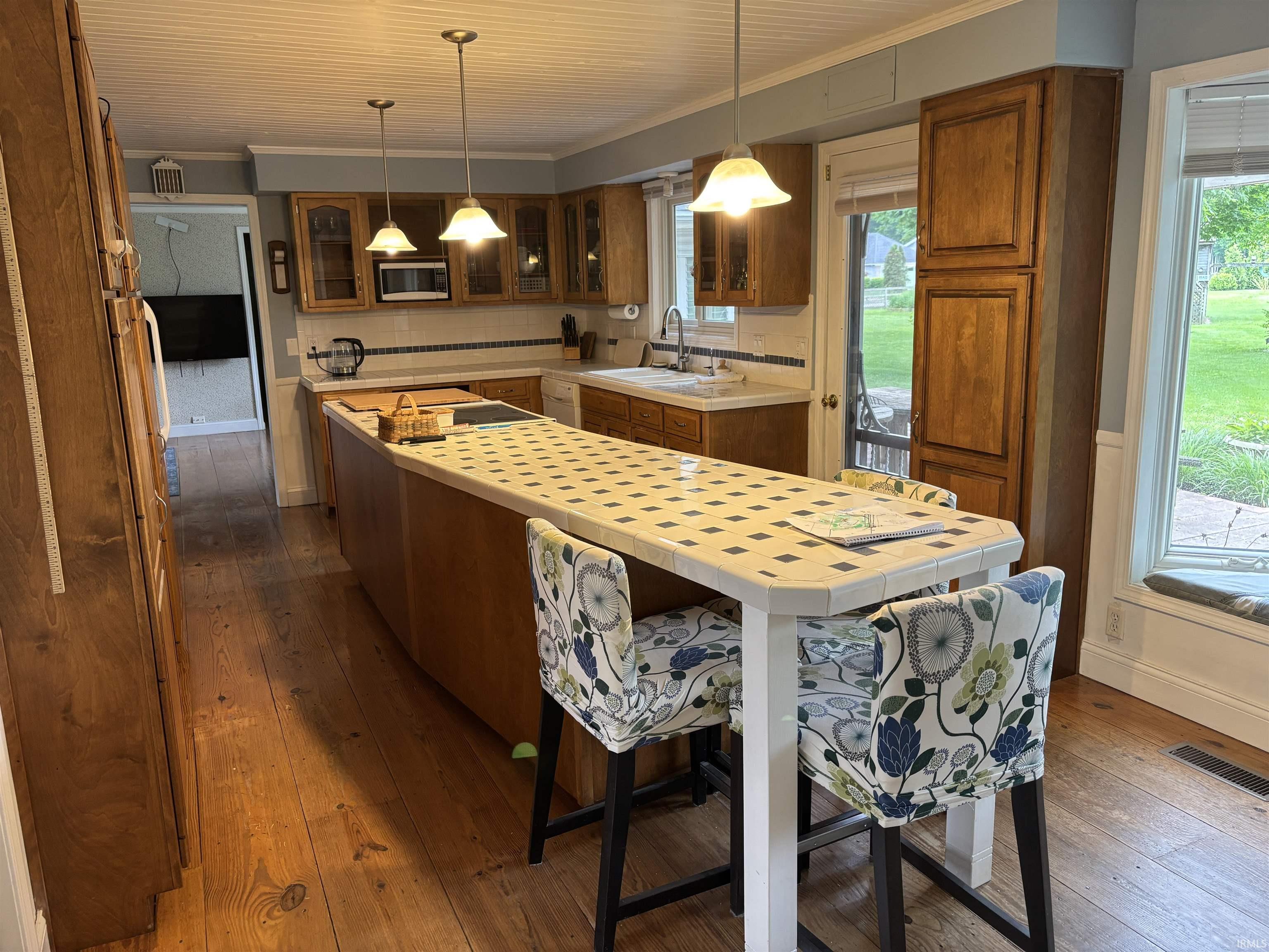 Kitchen featuring wood-finish flooring, a long island with a tiled countertop, wood cabinetry, and pendant lighting